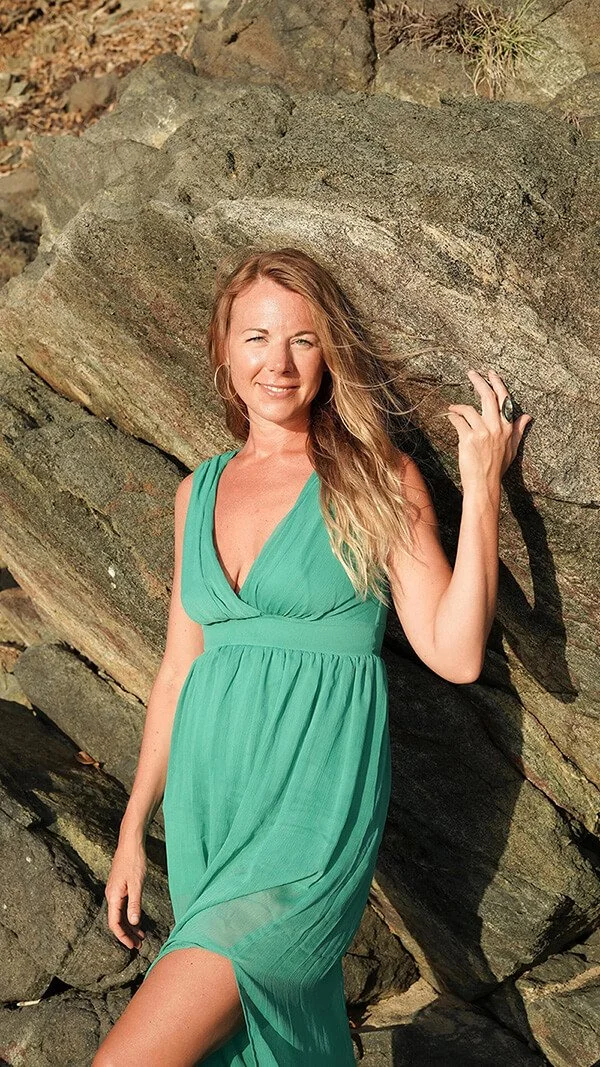A woman in a green dress leaning against rocks outdoors
