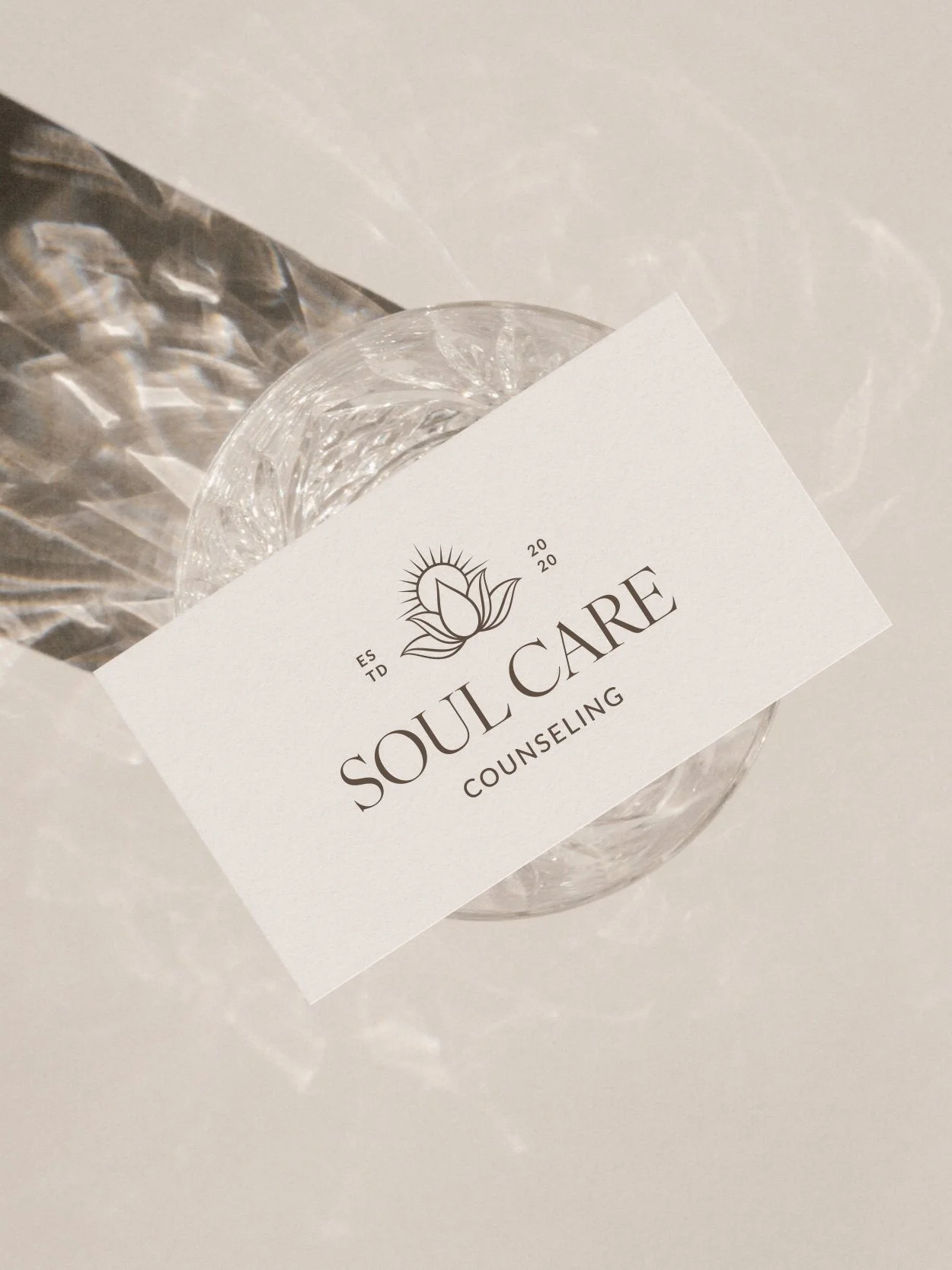 A glass of water with a Soul Care Counseling business card on top of it, placed on a white surface.
