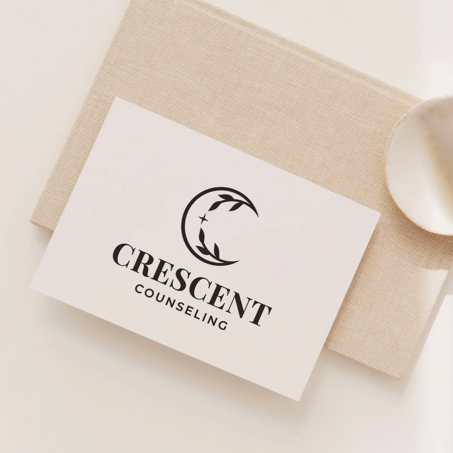 Business card for Crescents Counseling featuring a crescent moon with leaf and star designs, placed on textured beige paper with a white ceramic spoon nearby.