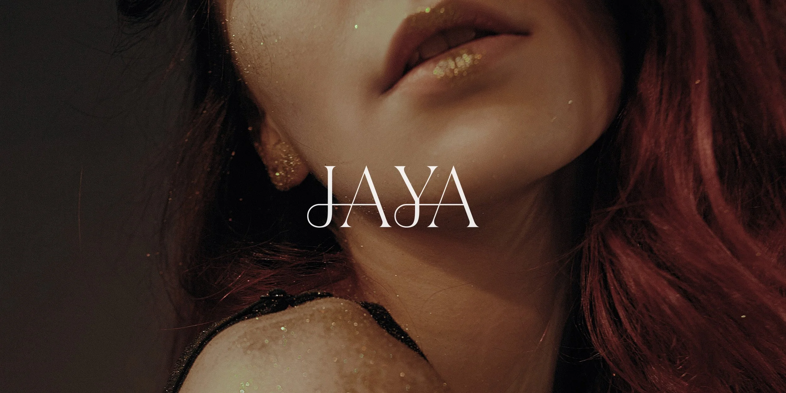 Close-up of a woman's face with red hair and glitter makeup, with the name 'JAYA' overlaid in white text.