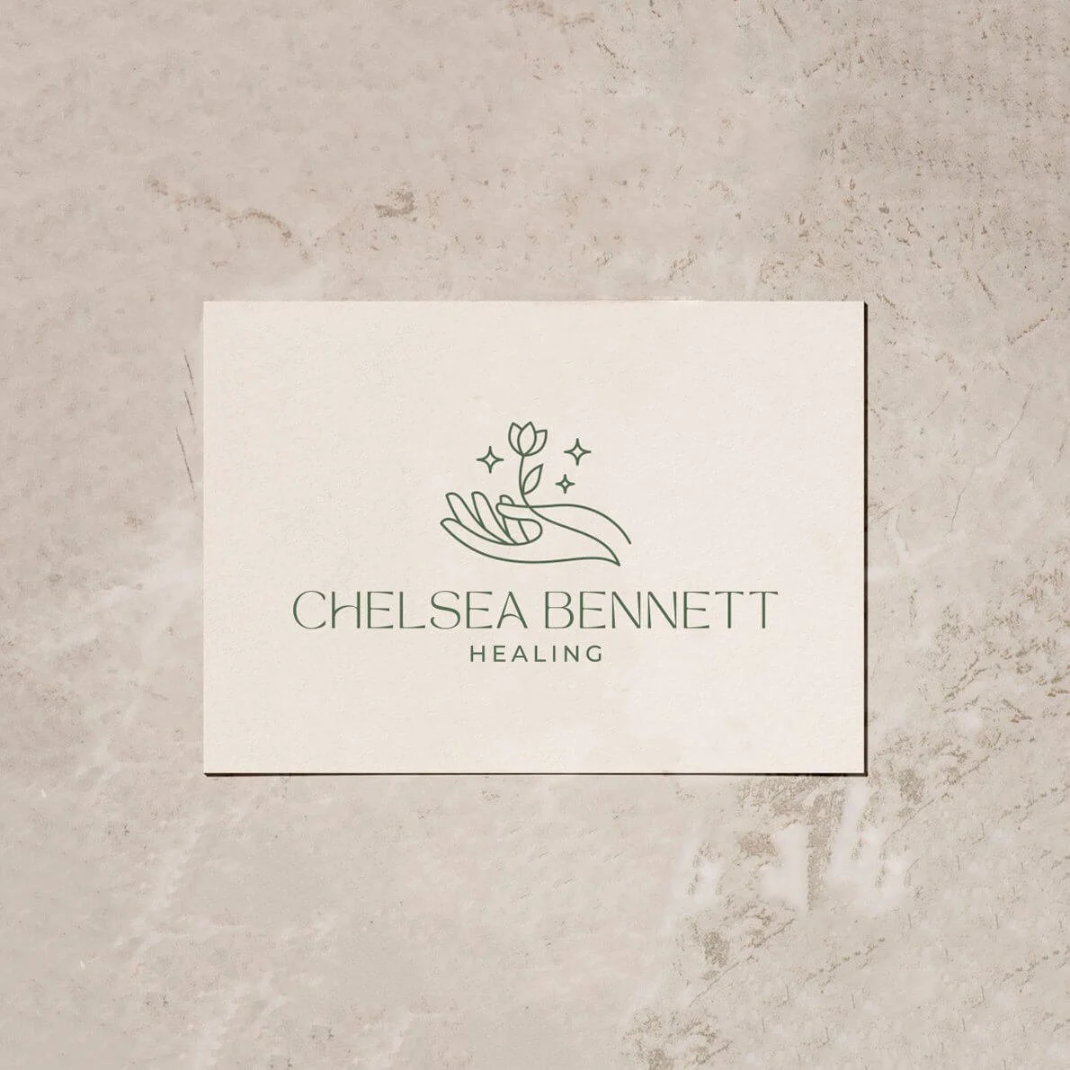 A business card with an illustration of a hand holding a flower, with stars around it, on a textured surface.