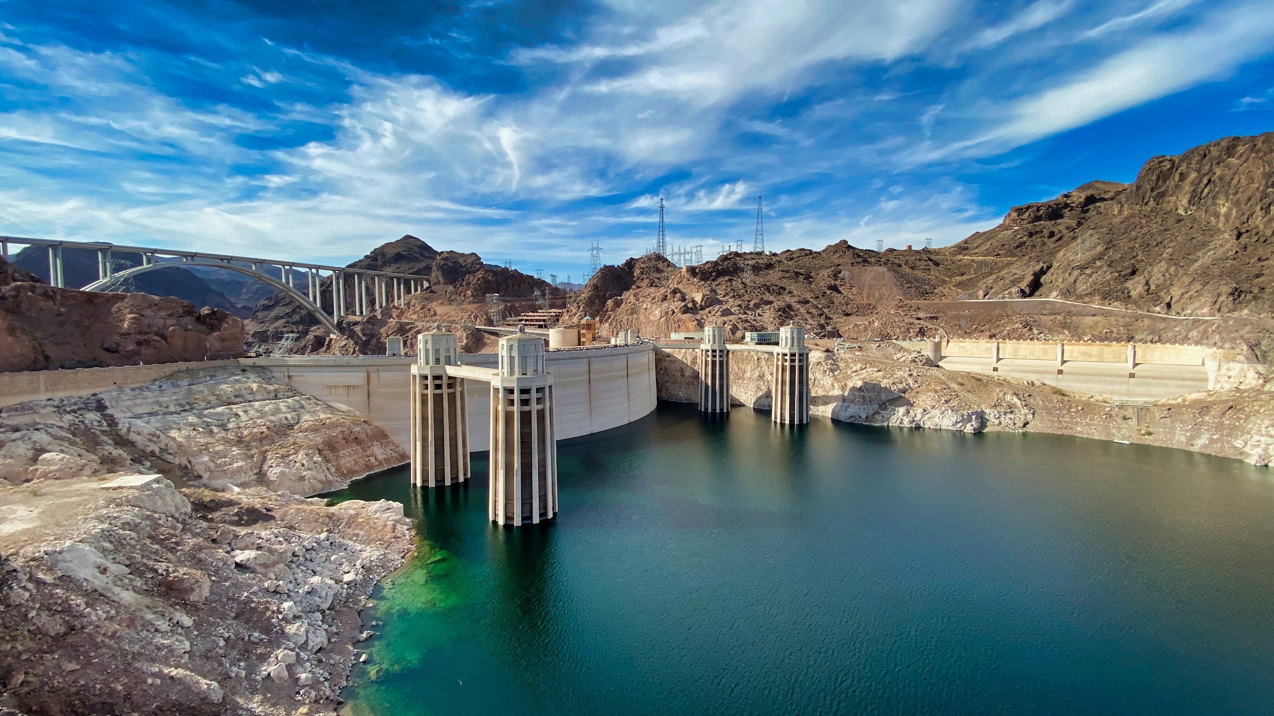 The Hoover Dam on the Colorado River in Nevada, with a partly cloudy sky and surrounding mountains.