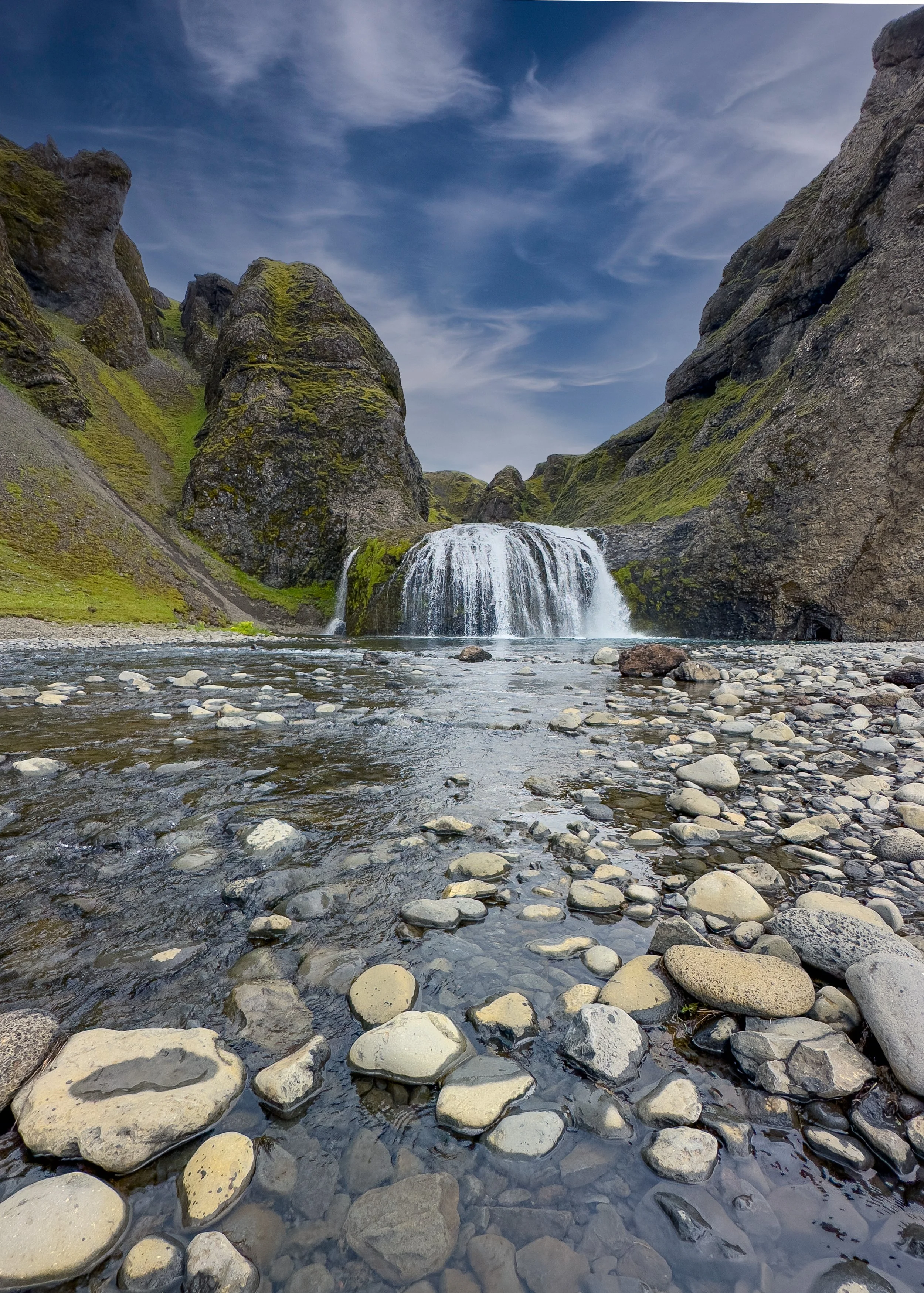Stjórnarfoss in Iceland is a scenic, multi-tiered waterfall flowing over dark volcanic cliffs into a flat riverbed, with green moss.