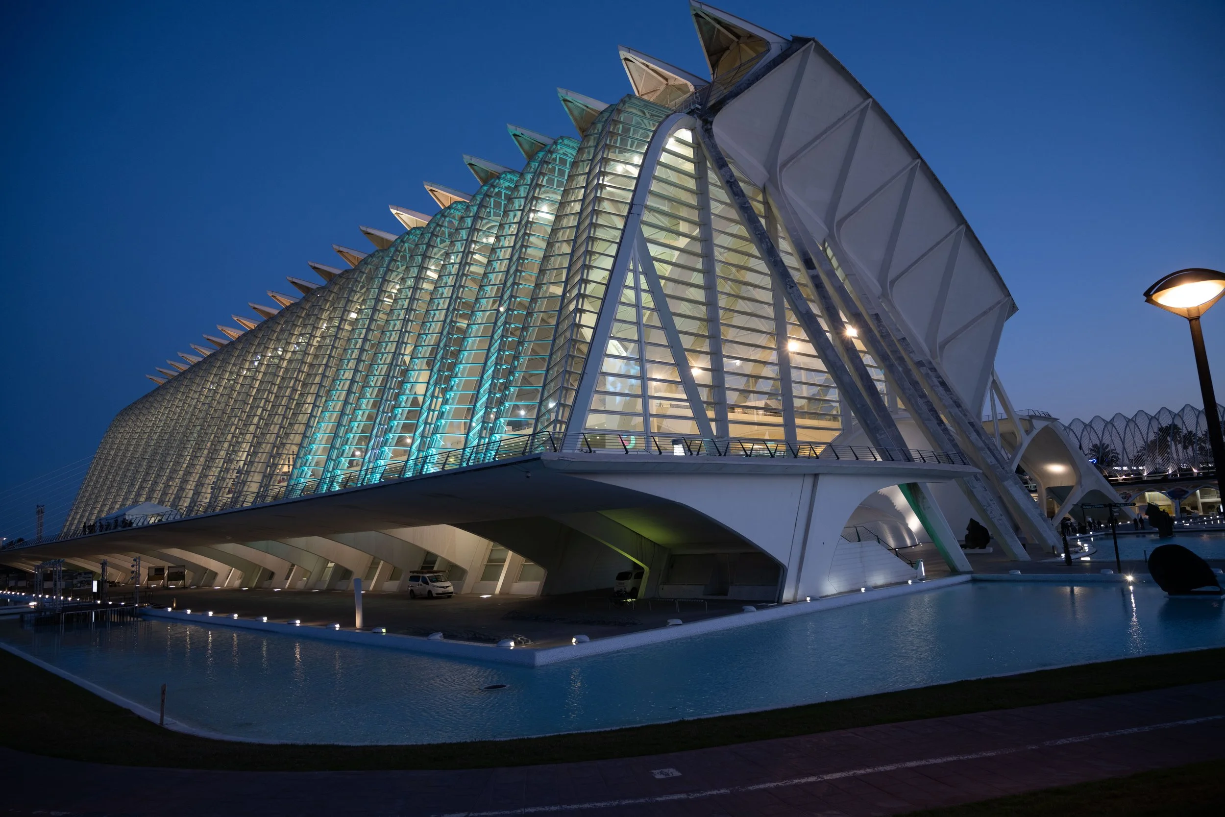 Modern architectural building with glass and metal structure, illuminated at night, with a water feature in the foreground.