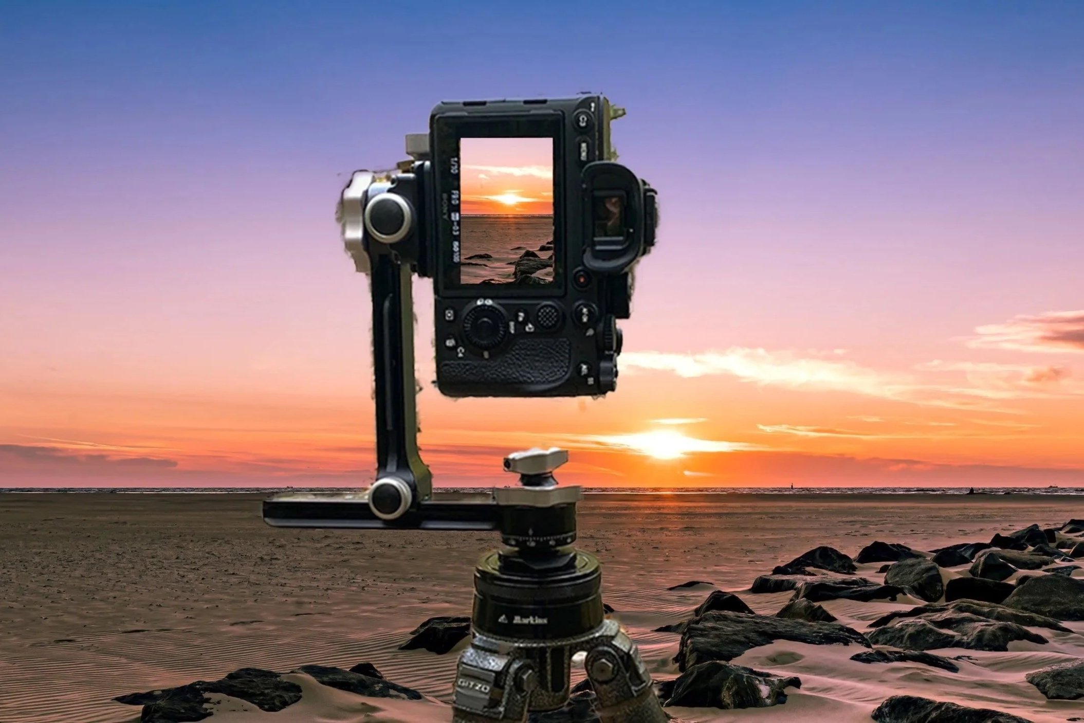 Camera mounted on a tripod capturing a sunset over the ocean at the beach with rocks in the foreground.