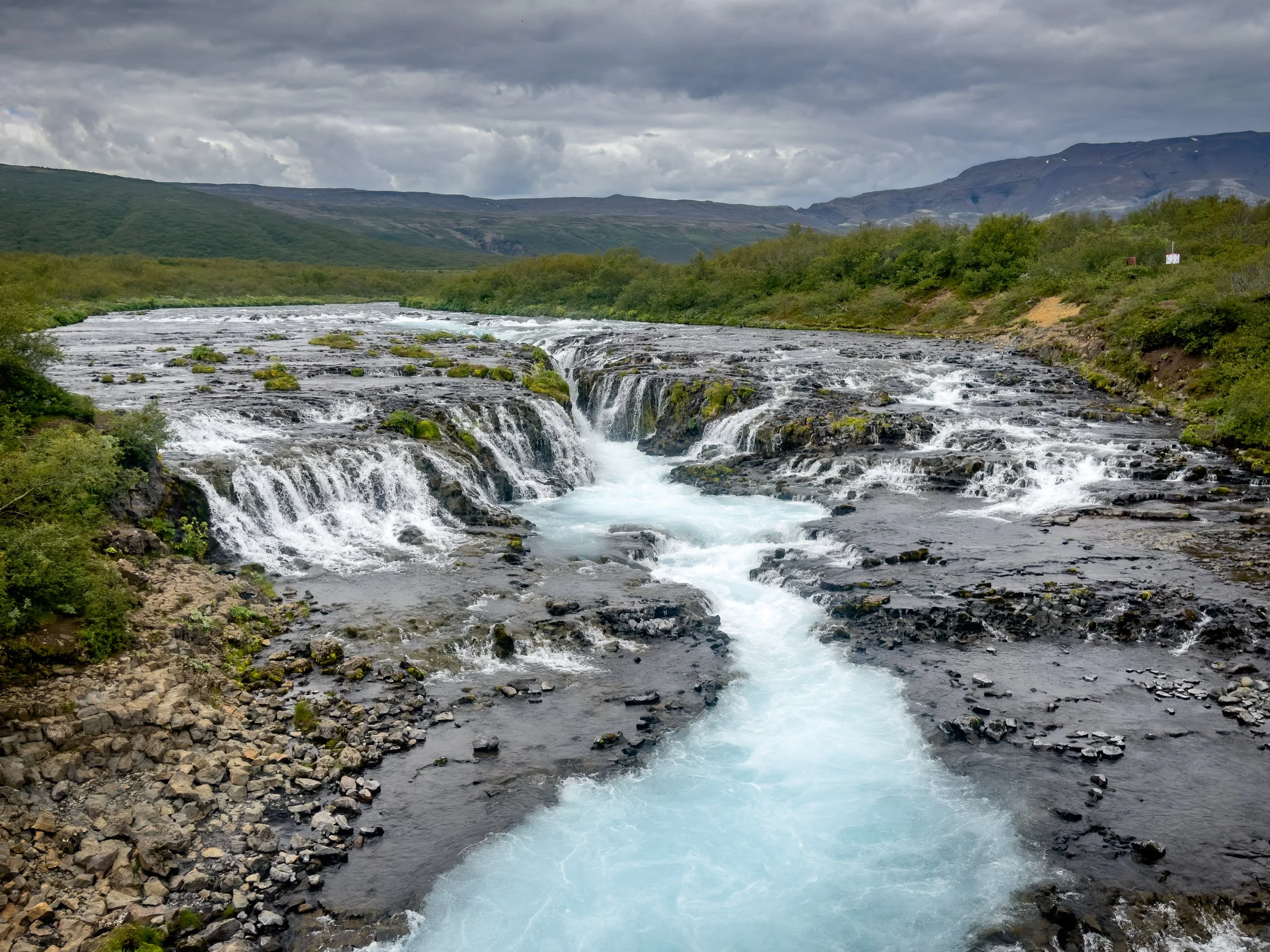 Panoramic view of the small but stunning Brúarfoss waterfall in Southern Iceland, showcasing its intense turquoise color against the rugged Icelandic landscape
