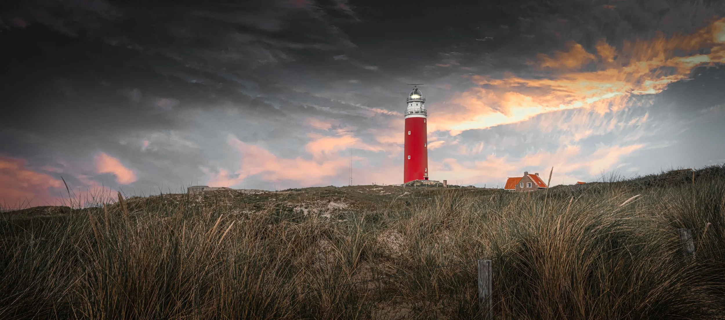 A red and white lighthouse standing on a grassy hill under a cloudy sunset sky.