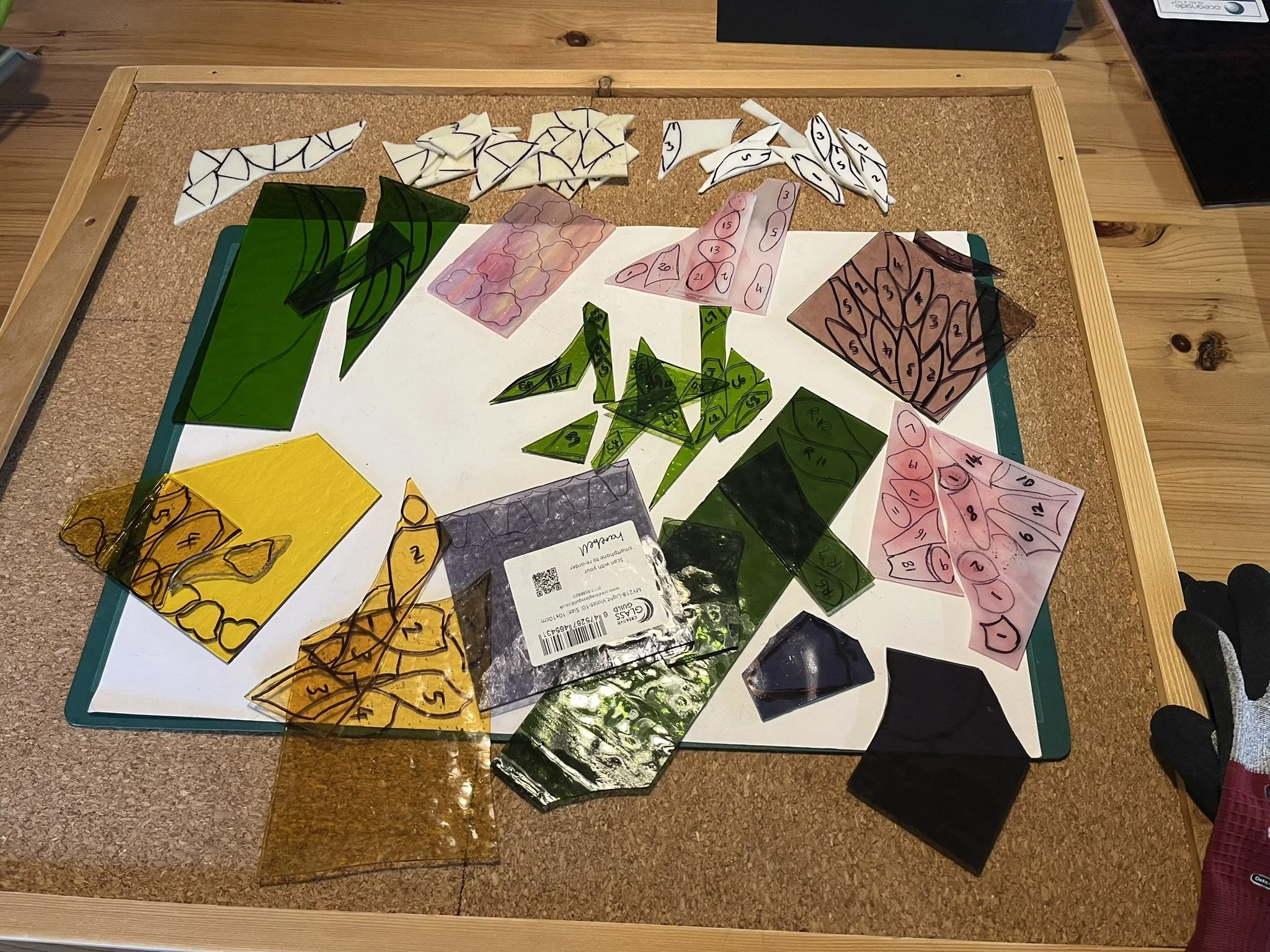 Colorful stained glass pieces with numbered patterns arranged on a white board on a wooden table.