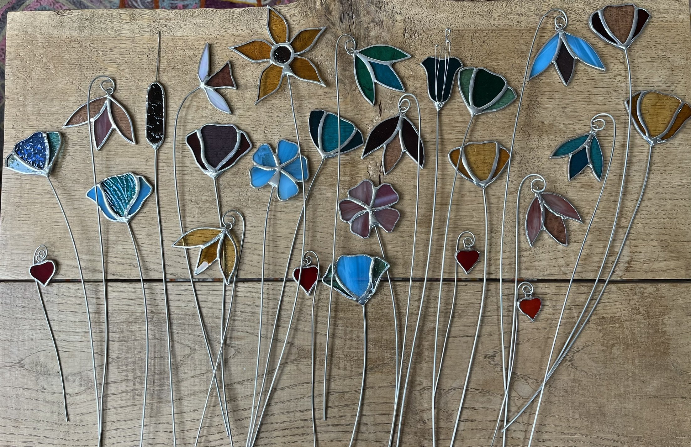 A collection of stained glass flower stems laid out on a wooden surface.
