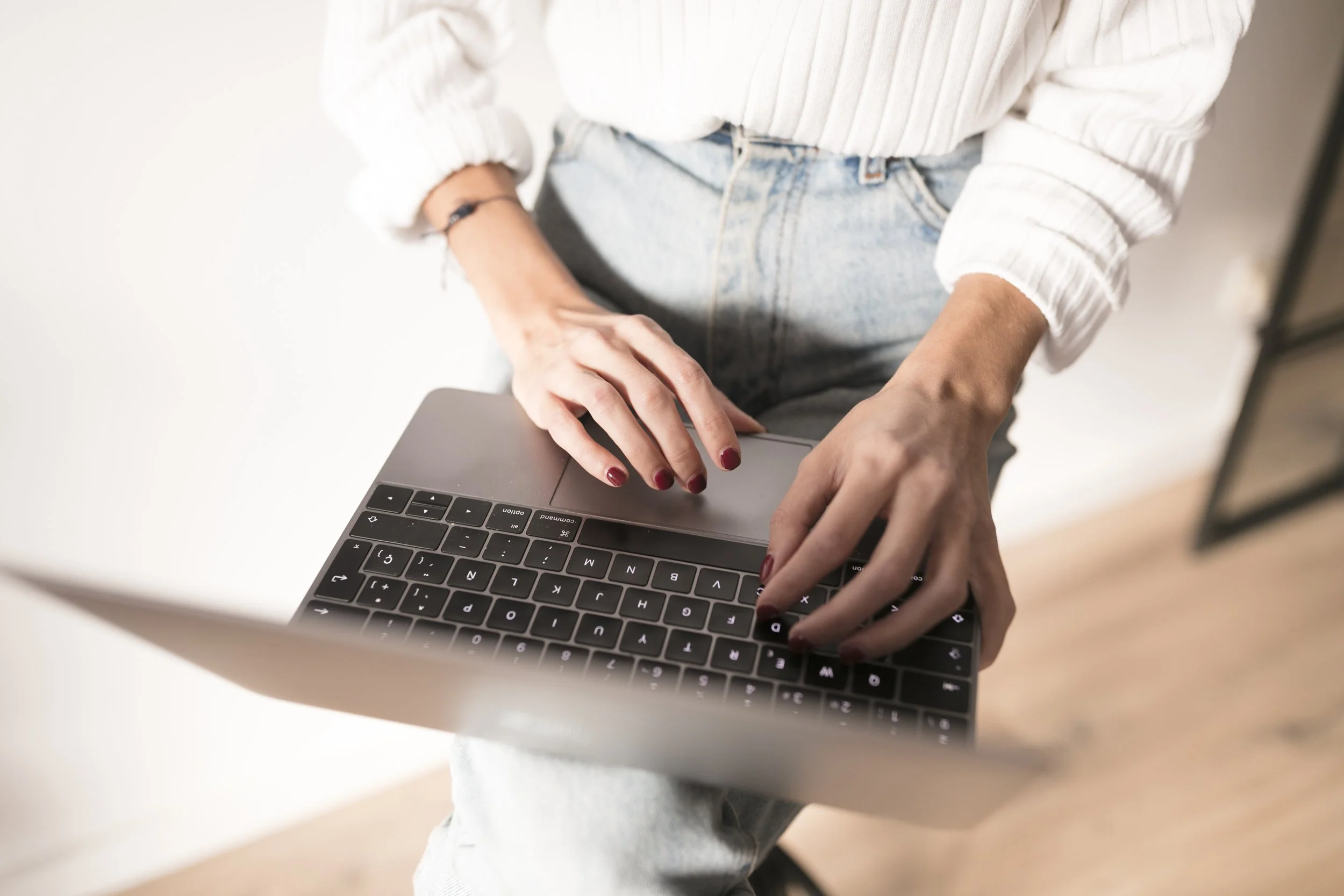 Persona usando laptop con uñas pintadas y chaqueta blanca a rayas