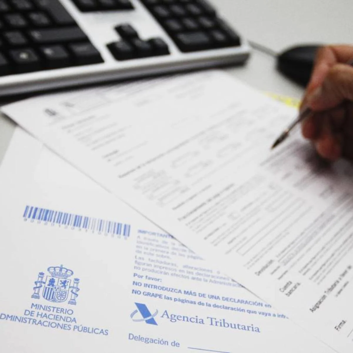 Documento oficial de la Agencia Tributaria y Ministerio de Hacienda de España, con firma y firma de autoridad, acompañado de un bolígrafo y teclado.