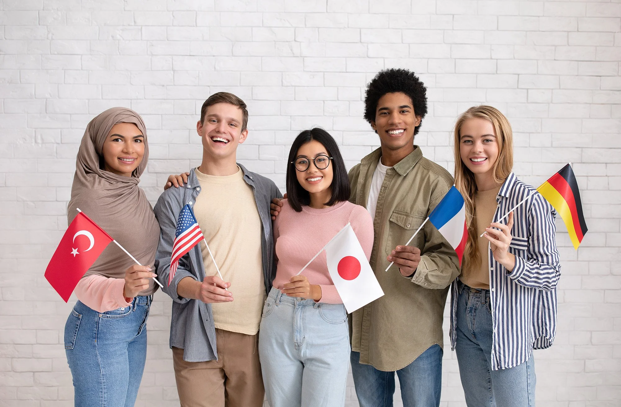 Grupo de seis jóvenes diversos sosteniendo banderas de diferentes países frente a una pared blanca, sonriendo y mostrando amistad y diversidad cultural.