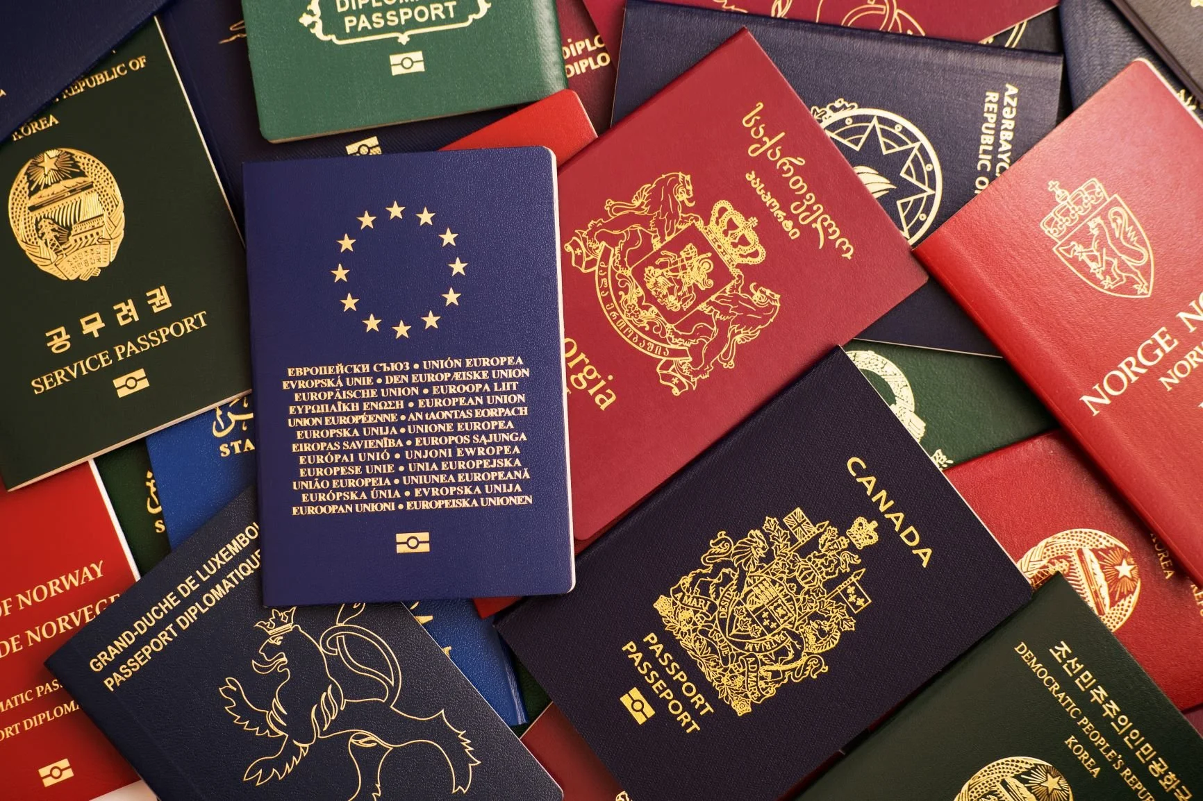 Varias pasaportes de diferentes países apilados, incluyendo Estados Unidos, Japón, Noruega, Canadá, y otros, con diferentes colores y diseños