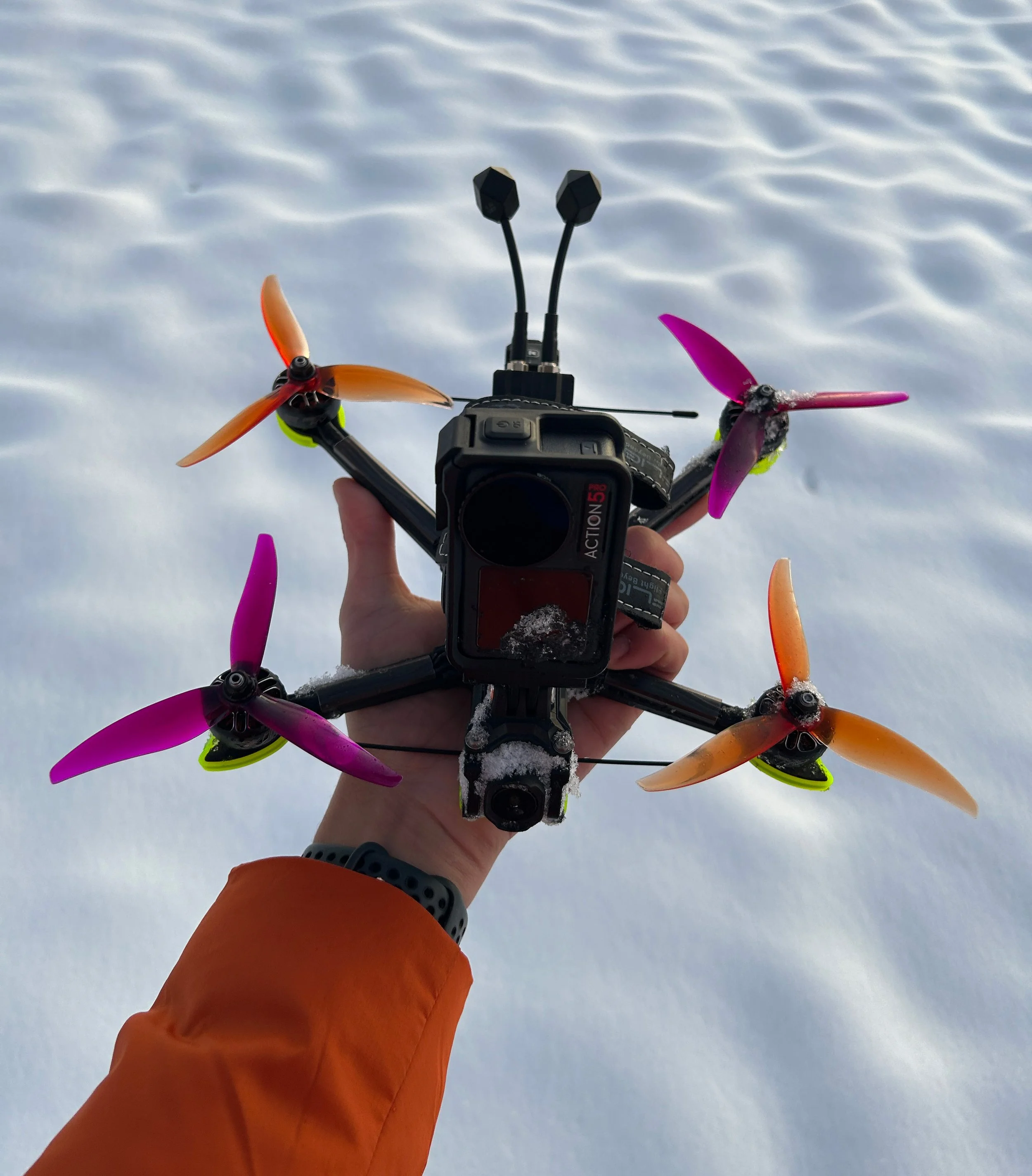 A person holding a drone with four propellers over a snowy landscape.
