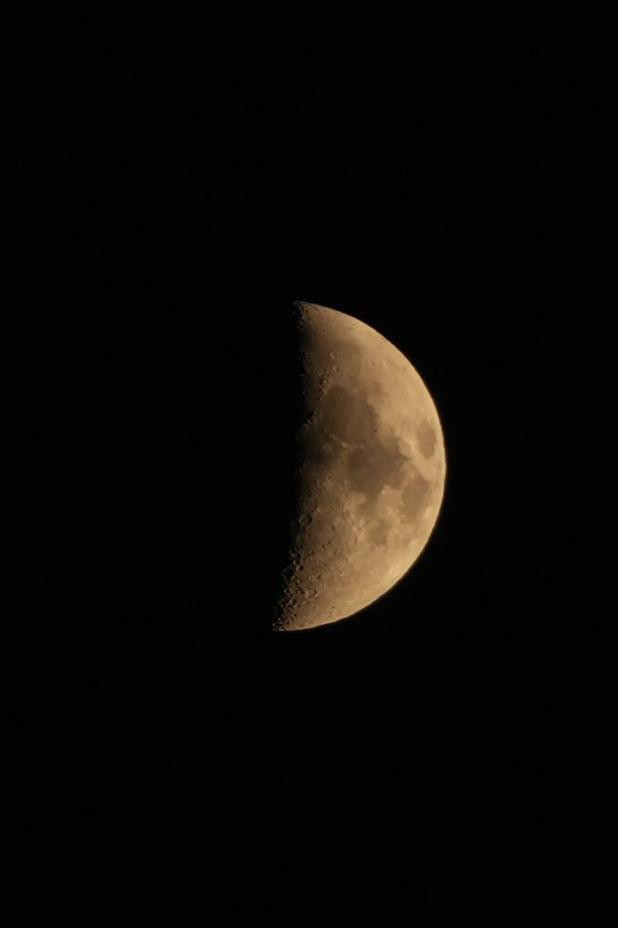 A photograph of the moon in its waxing phase, showing one half illuminated and the other half in shadow, set against a black night sky.