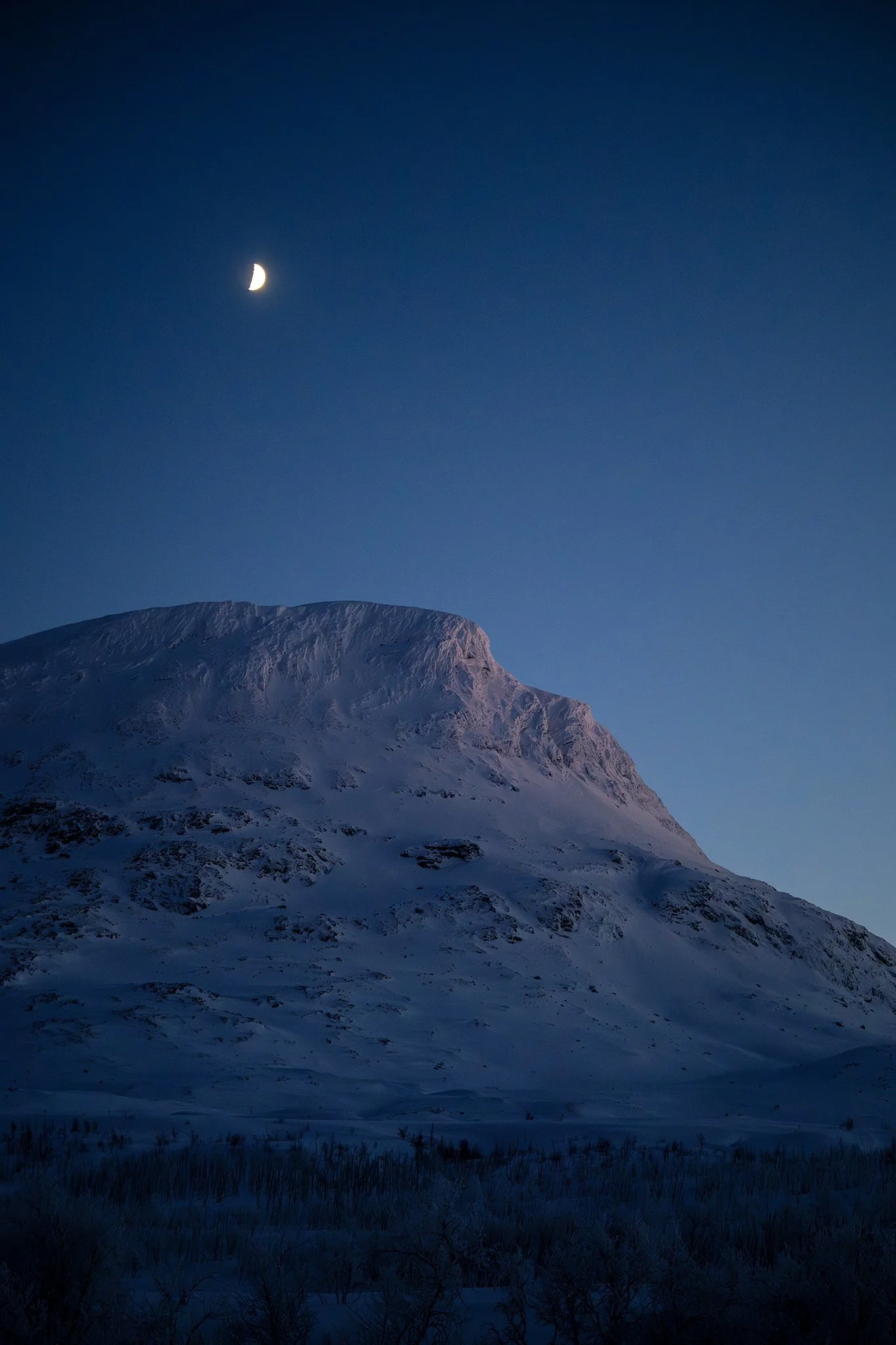 Snow-covered mountain under a dark blue sky with a crescent moon.