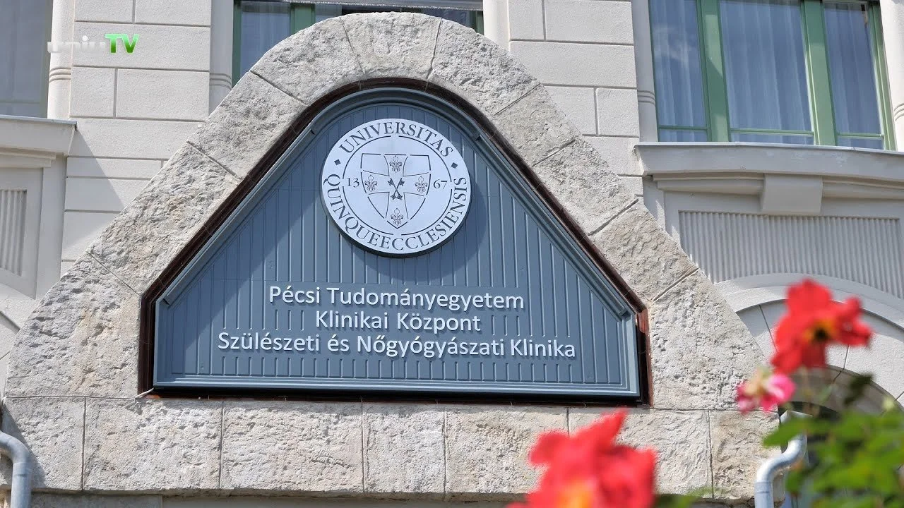 A sign on a stone archway of a building displaying the emblem and text for Pécsi Tudományegyetem Klinikai Központ Szülészeti és Nőgyógyászat Klinika, which translates to University of Pécs Clinical Center Obstetrics and Gynecology Clinic.