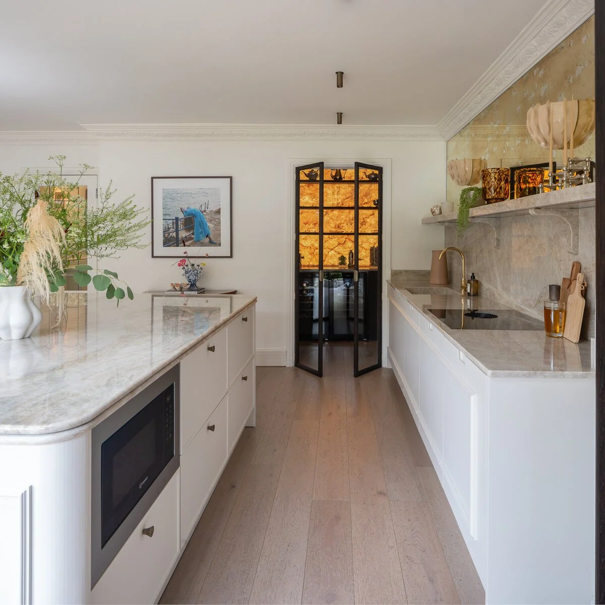 Painted galley kitchen with marble worktops and an illuminated drinks cabinet.