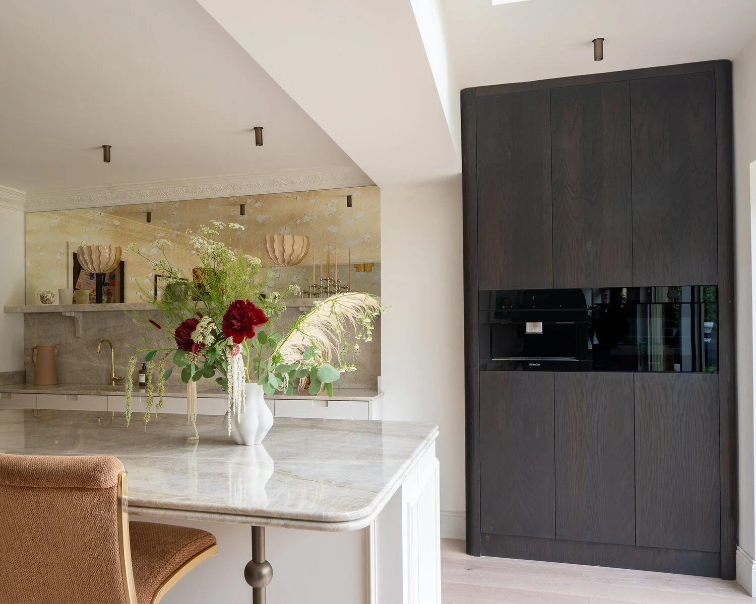 Painted kitchen with marble island and dark oak integrated appliance cabinetry.