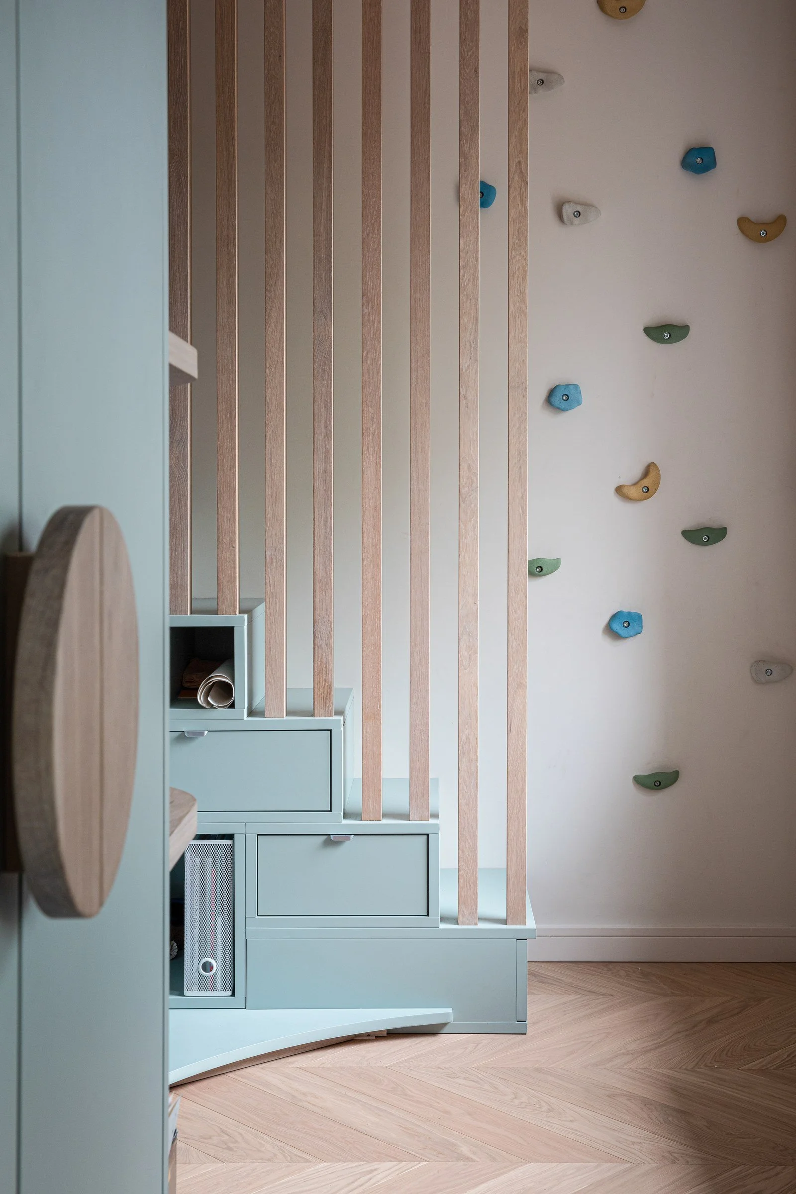 Playroom climbing wall with pastel storage, timber slats and integrated steps.