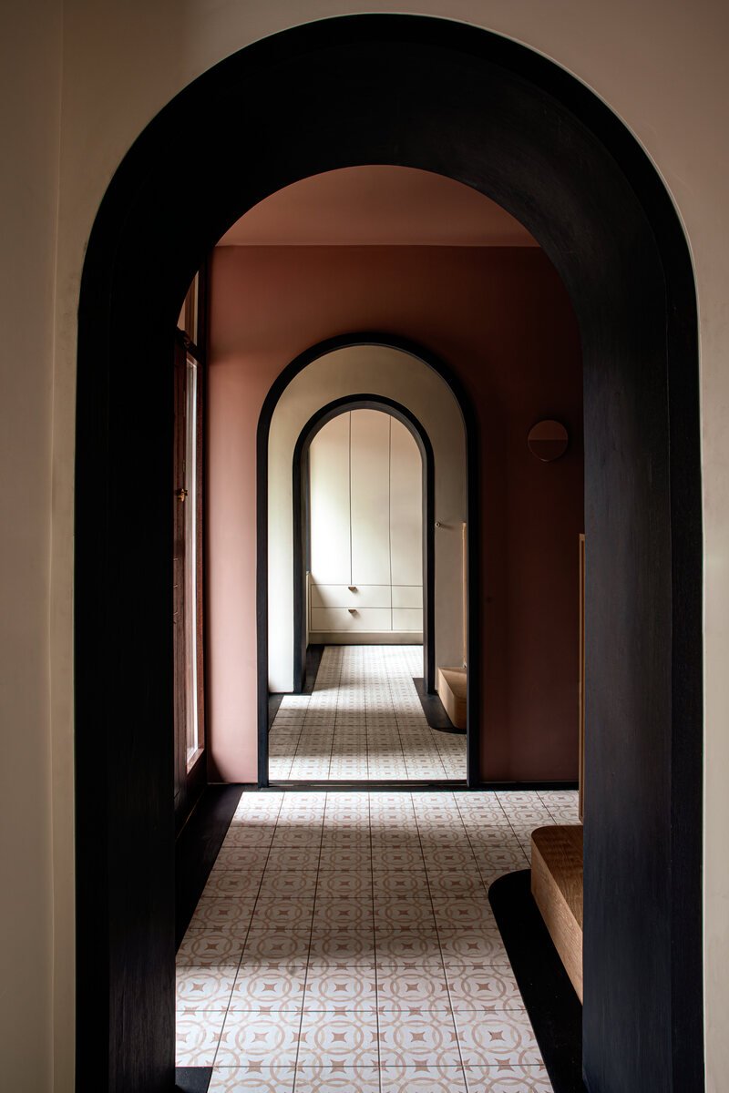 Terracotta hallway with arched doorway and bespoke mirrored joinery.