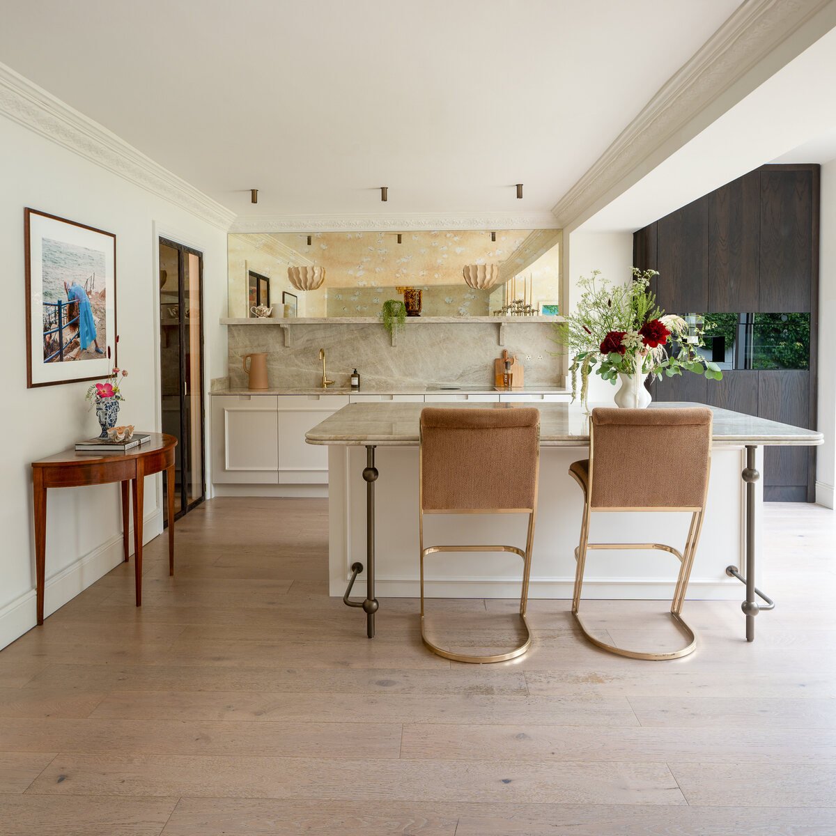 Painted kitchen with marble island, upholstered stools and dark oak cabinetry.
