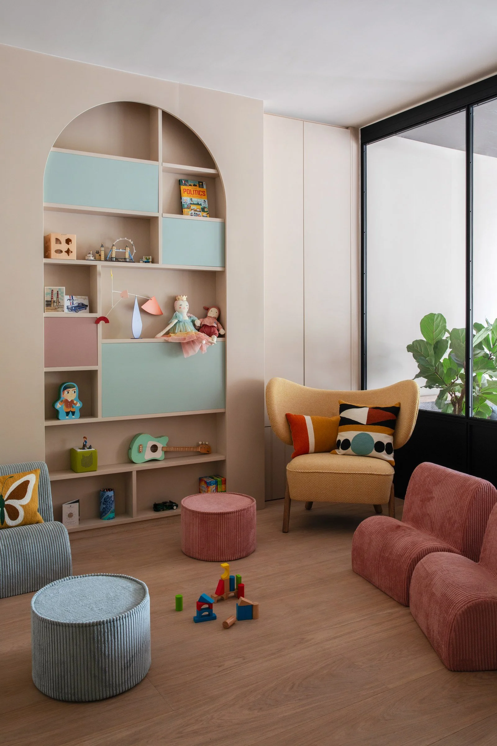 Children's playroom with pastel fitted storage, open shelving and a reading chair.