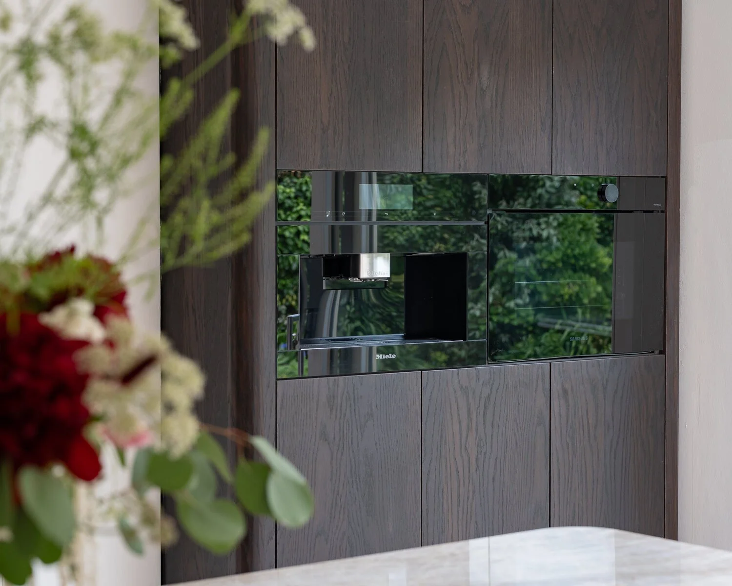 Dark oak appliance wall with integrated ovens and reflective glass detailing.