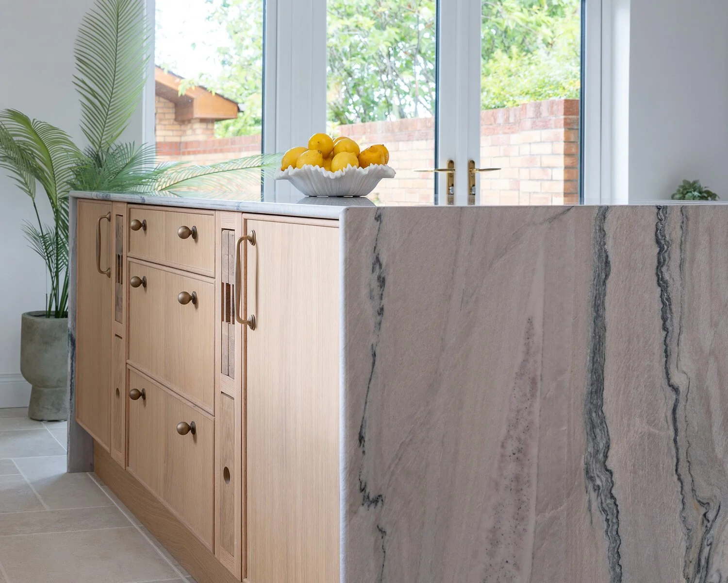Natural oak kitchen island with book-matched stone end panel and brass hardware.