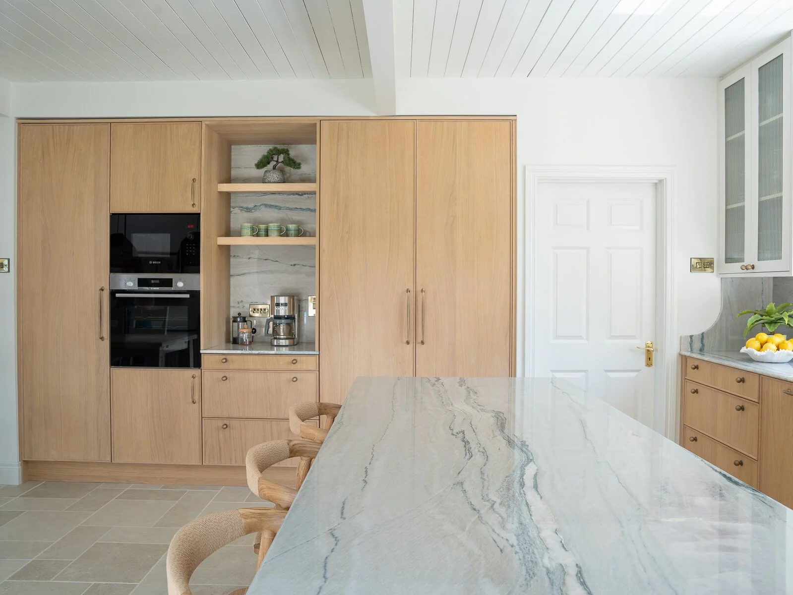 Natural oak kitchen with integrated appliances, coffee station and veined stone island.