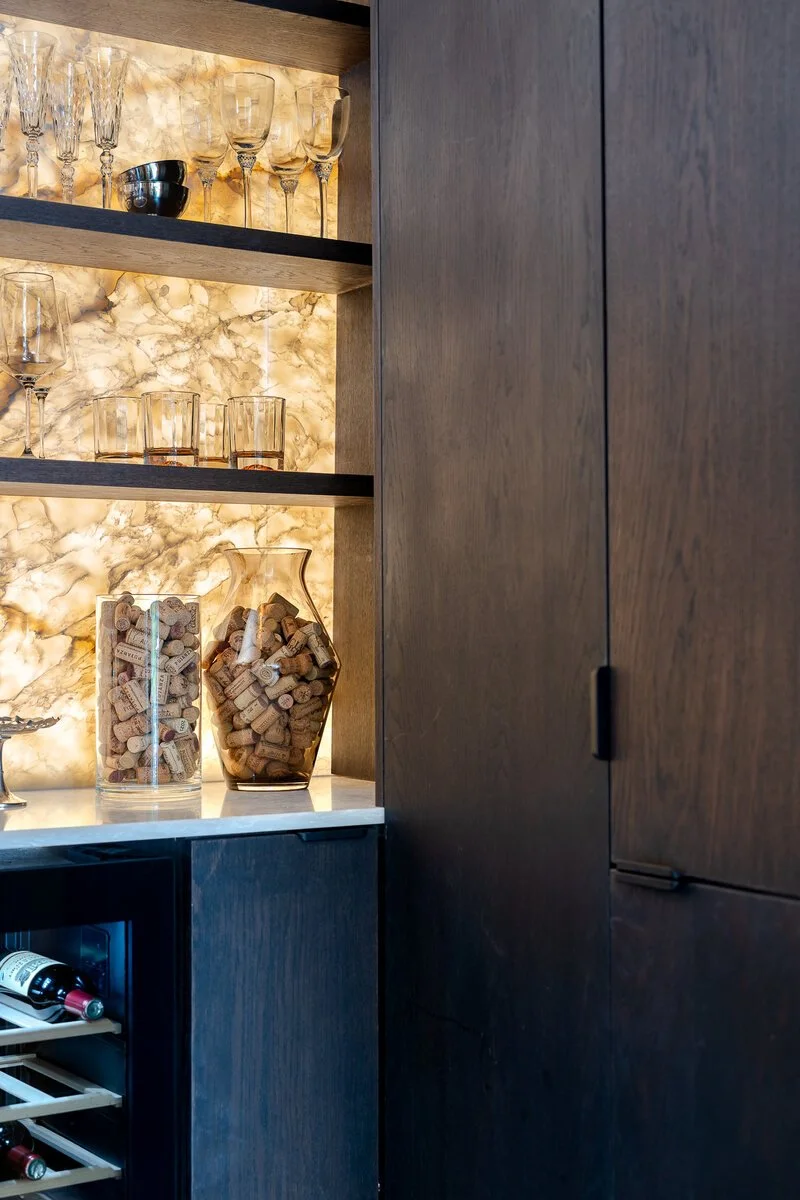 Dark oak drinks cabinetry with illuminated stone shelving by Royal & Co.