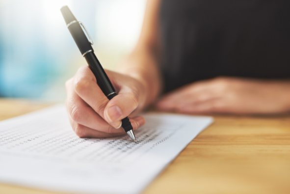 A person holding a black pen and signing a document on a wooden table.