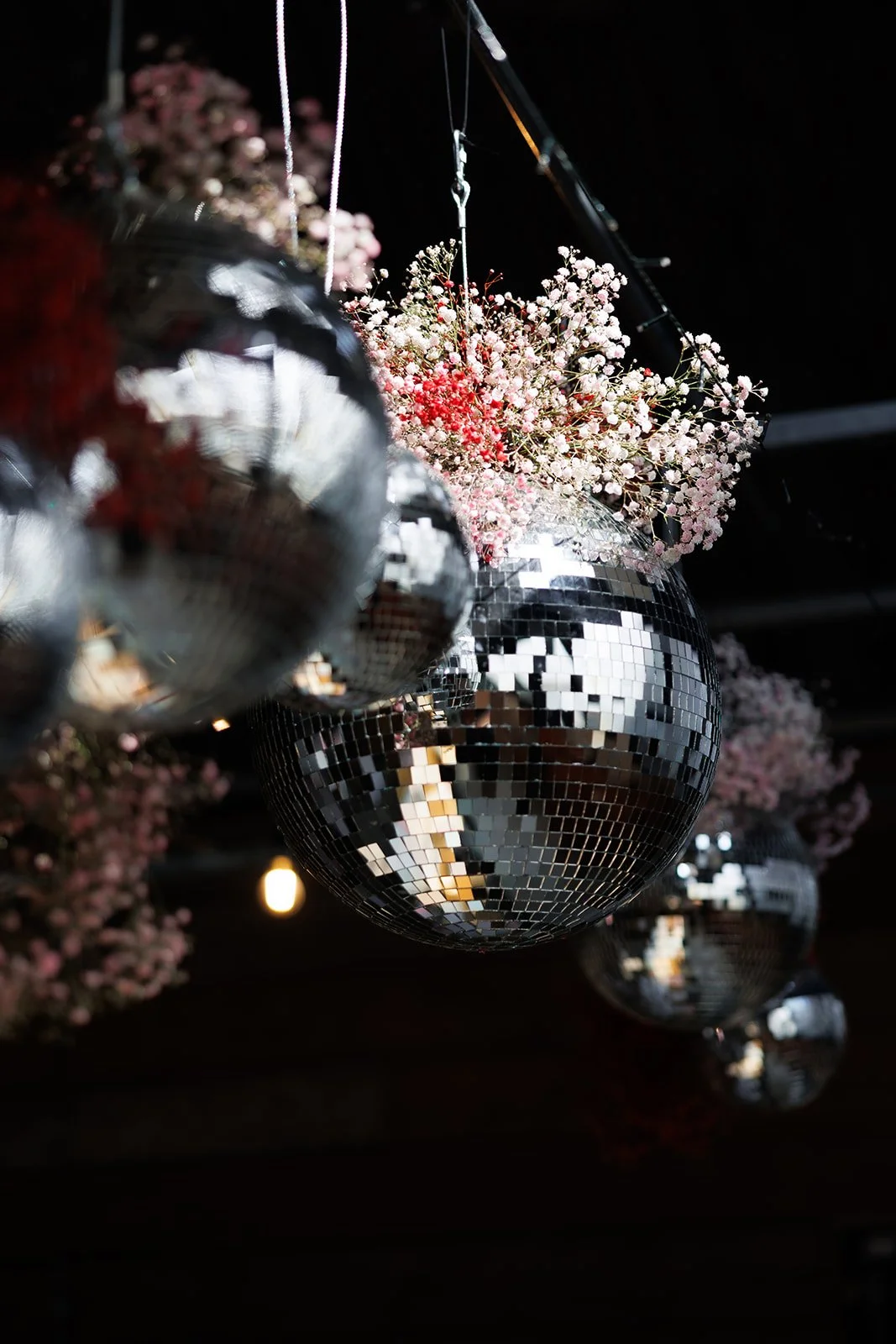 Multiple disco balls hanging from the ceiling, reflecting light, with pink and white flowers in the background.
