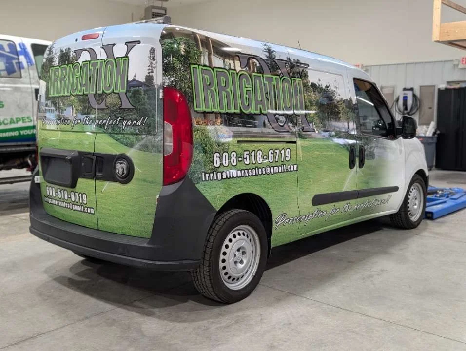 A commercial van with a green and black wrap advertising irrigation services, featuring contact information and the company slogan.