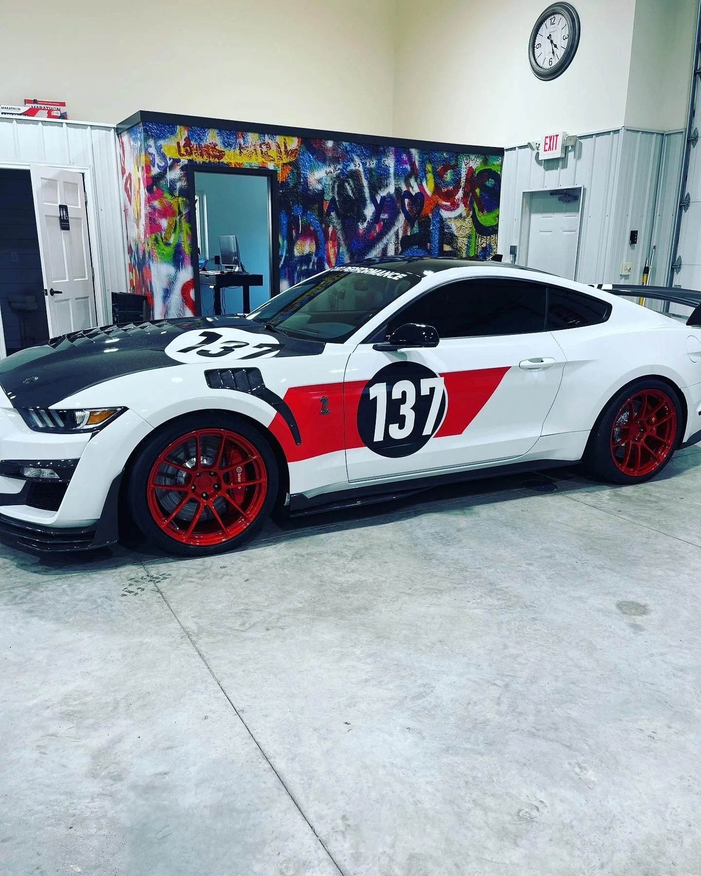 A white race car with red wheels and racing number decals parked indoors against a colorful graffiti wall.