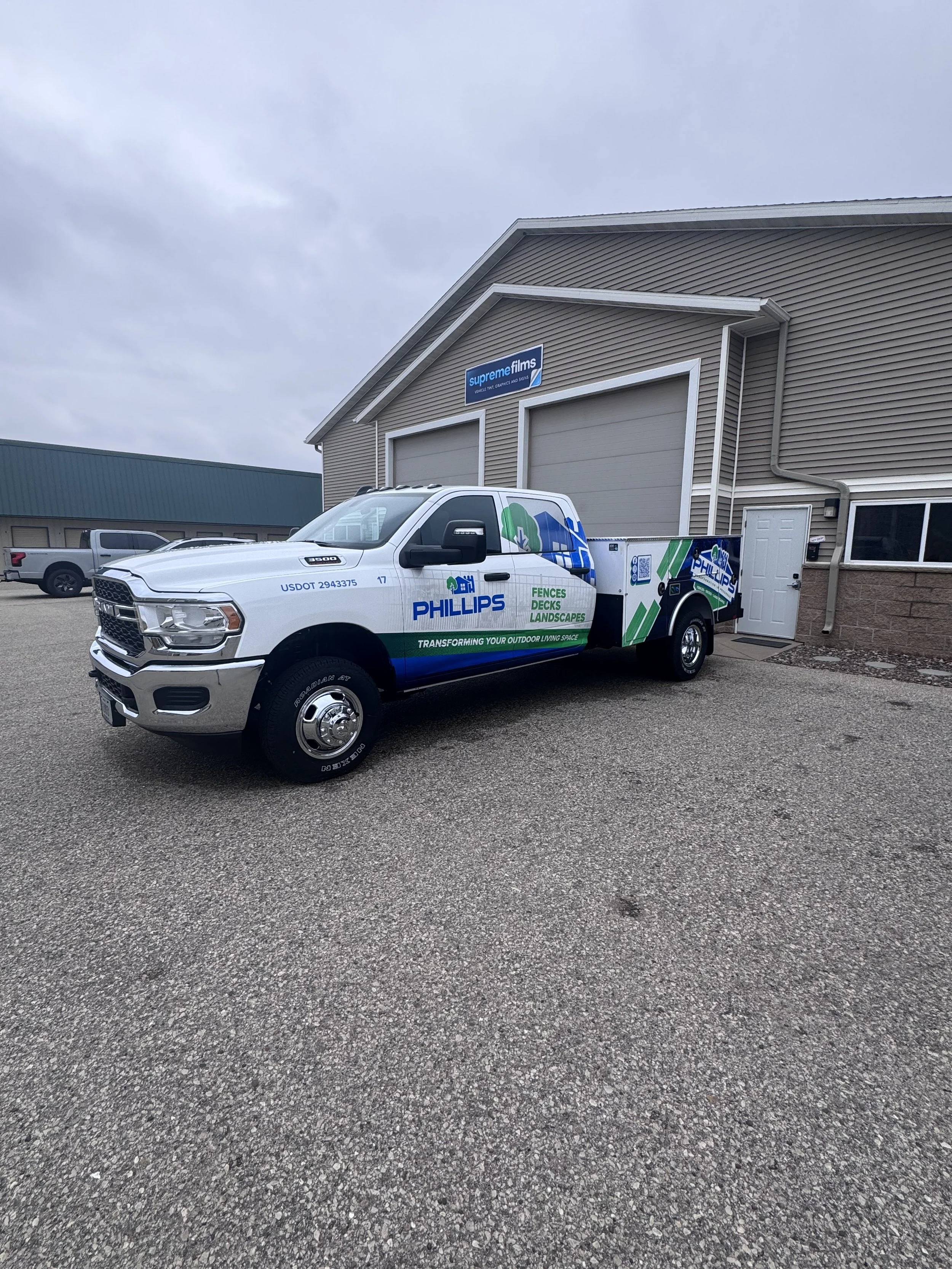 A fleet maintenance truck with Phillips landscaping branding parked outside a building with a sign that says 'supreme films' on a cloudy day.