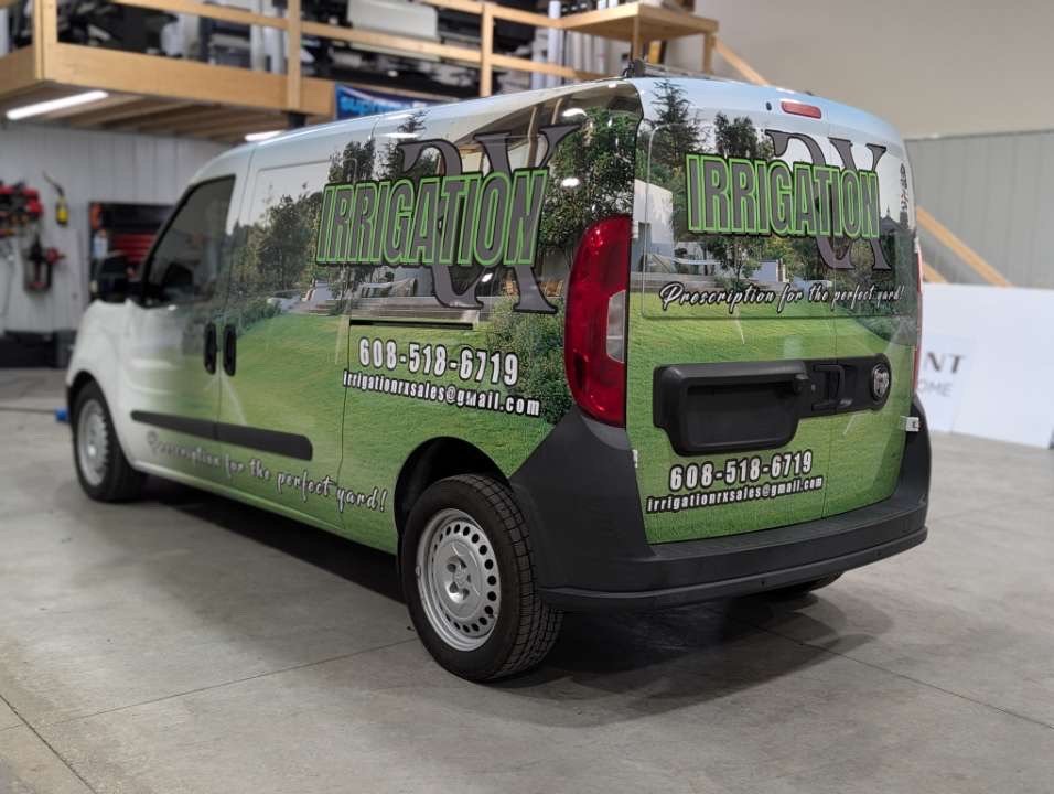 A company van displaying green and black graphics for irrigation services, including contact information, parked indoors on a concrete floor.