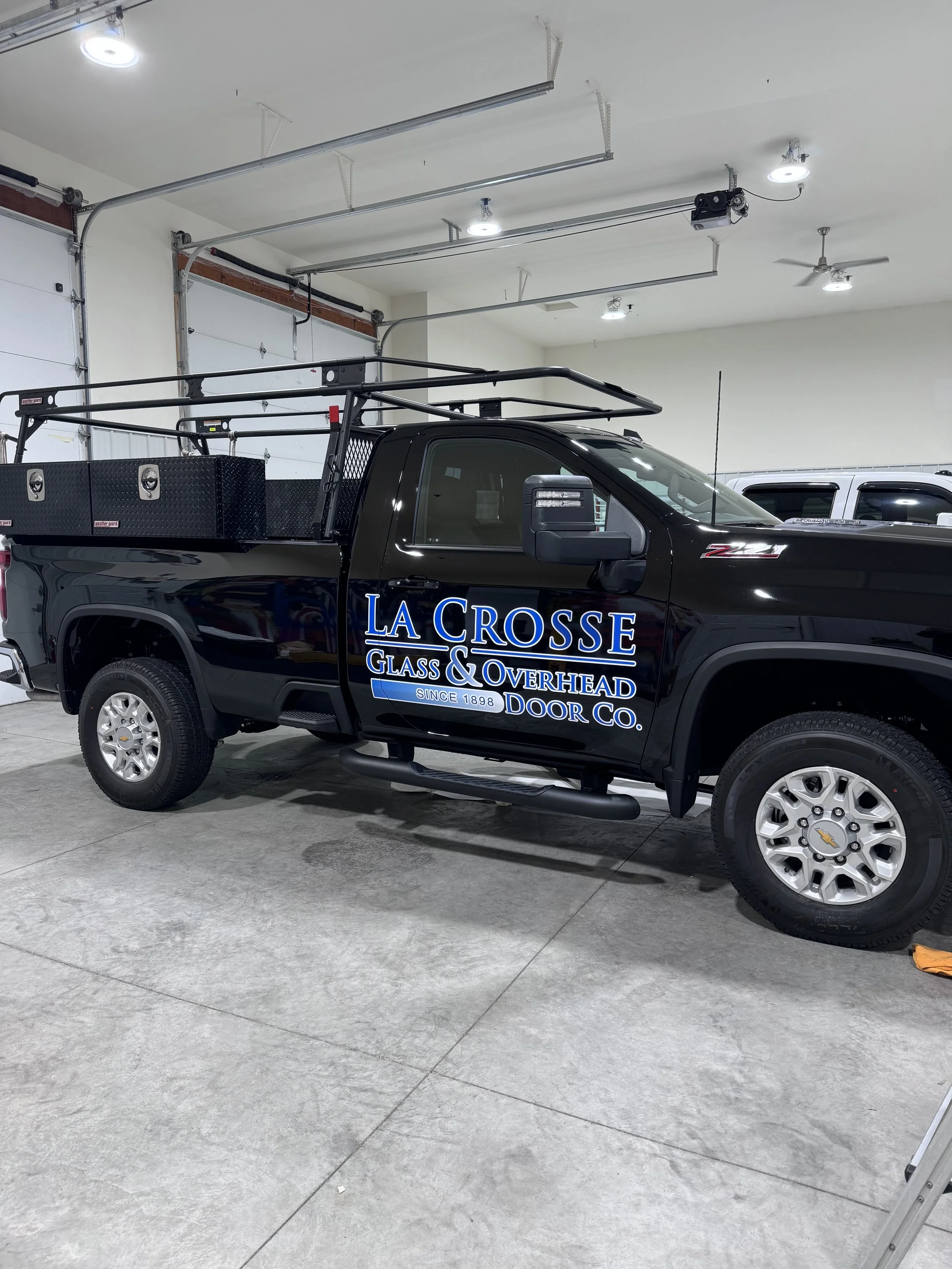 Black pickup truck with company logo for La Crosse Glass & Overhead Door Co. parked inside a garage.