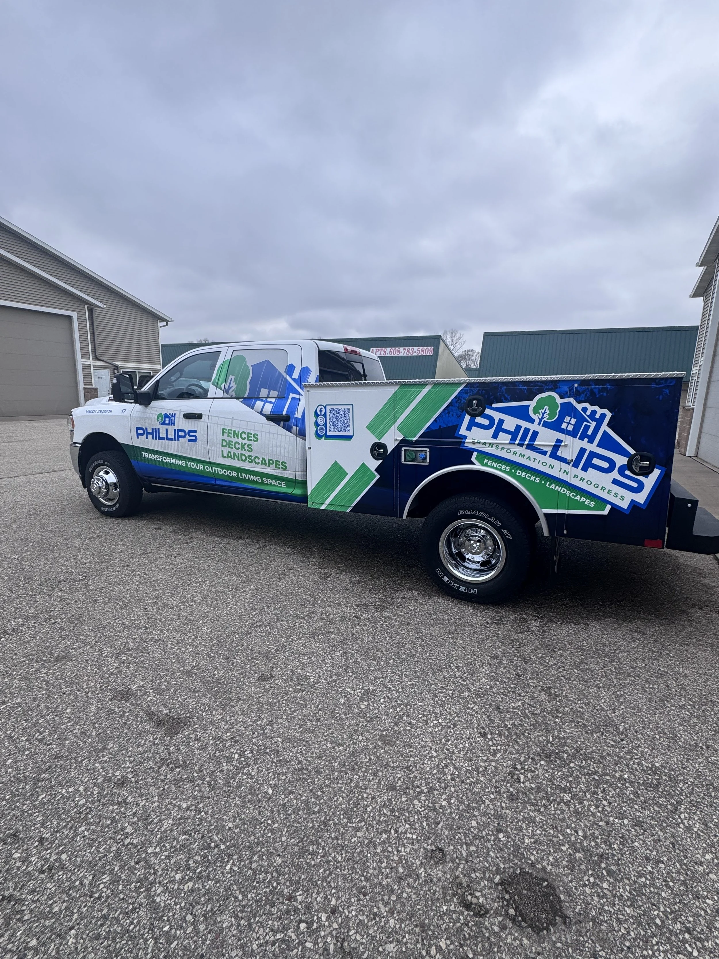 Company truck with Phillips Landscaping branding, parked outdoors near residential buildings under cloudy skies.