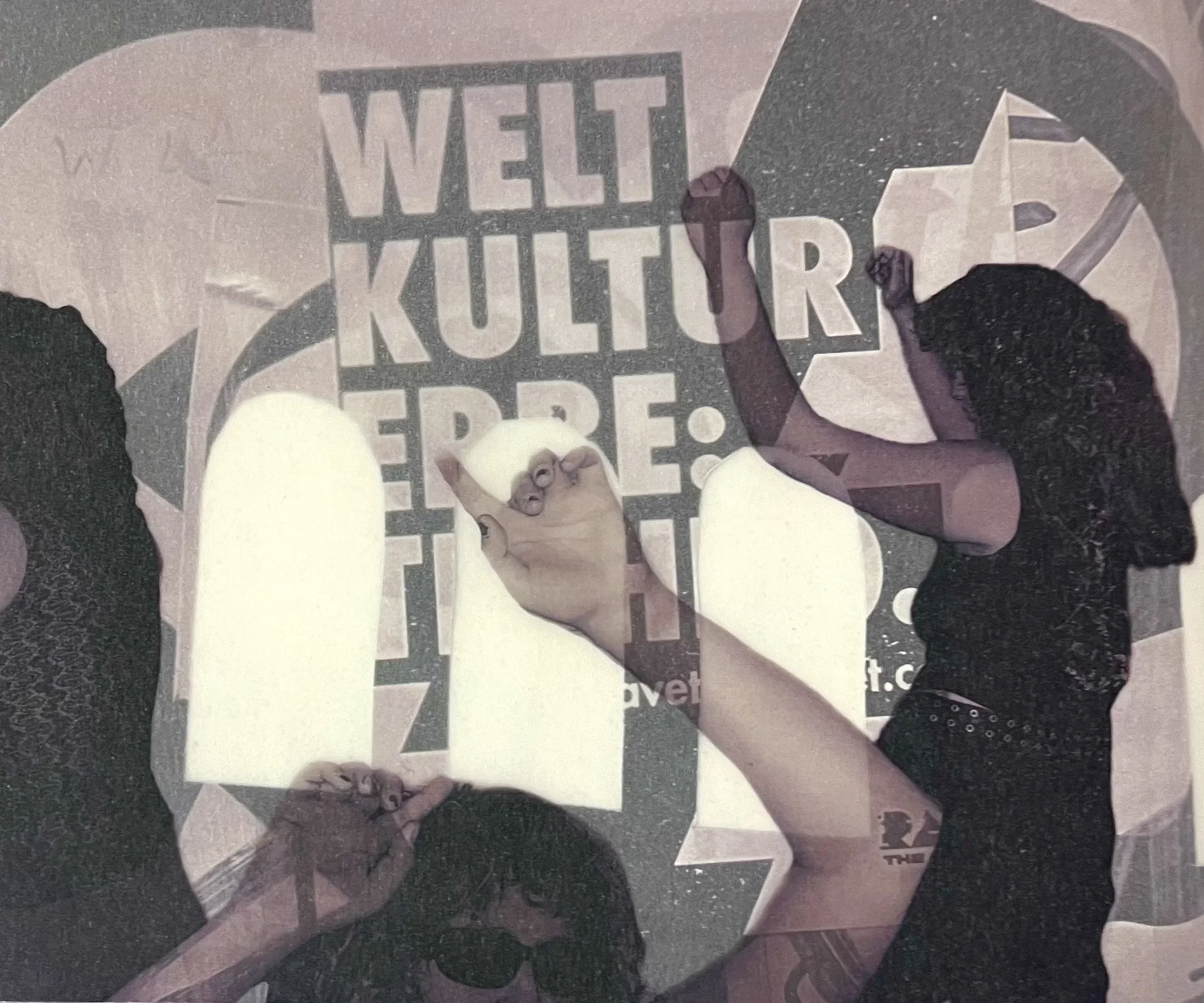 Multiple people with their fists raised in front of a sign that reads 'WELT KULTUR ERFE'.