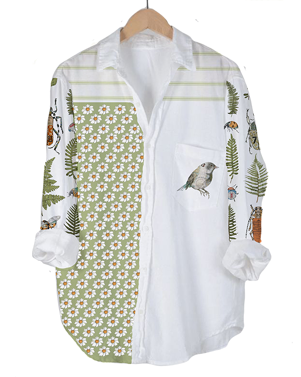 A white button-up shirt with a patchwork design featuring floral, animal, and foliage motifs, displayed on a hanger.
