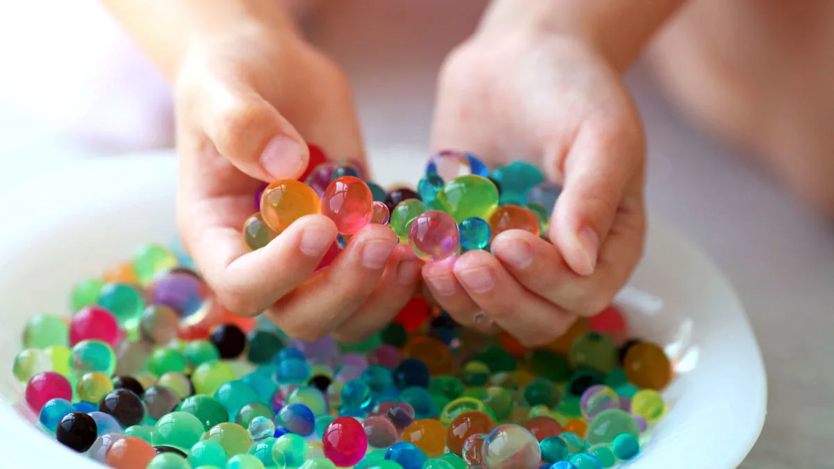 Hands holding colorful water beads over a bowl filled with more water beads.