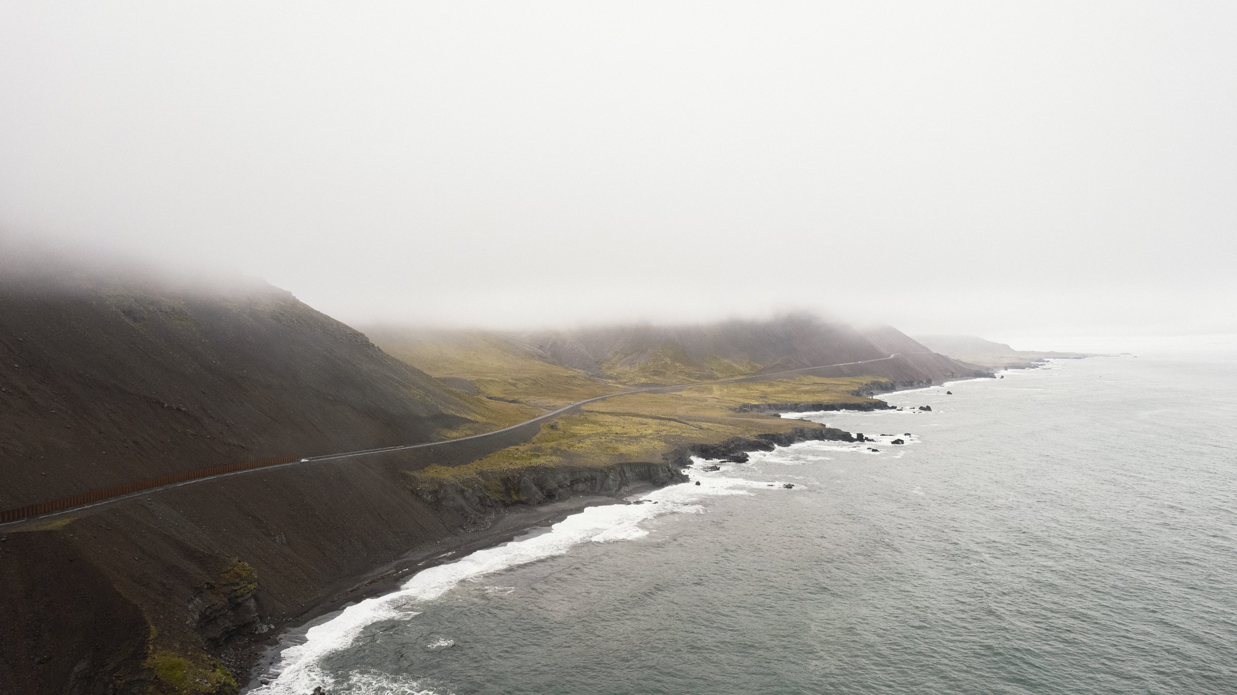 Coastal road along a foggy, rocky shoreline with hills in the background