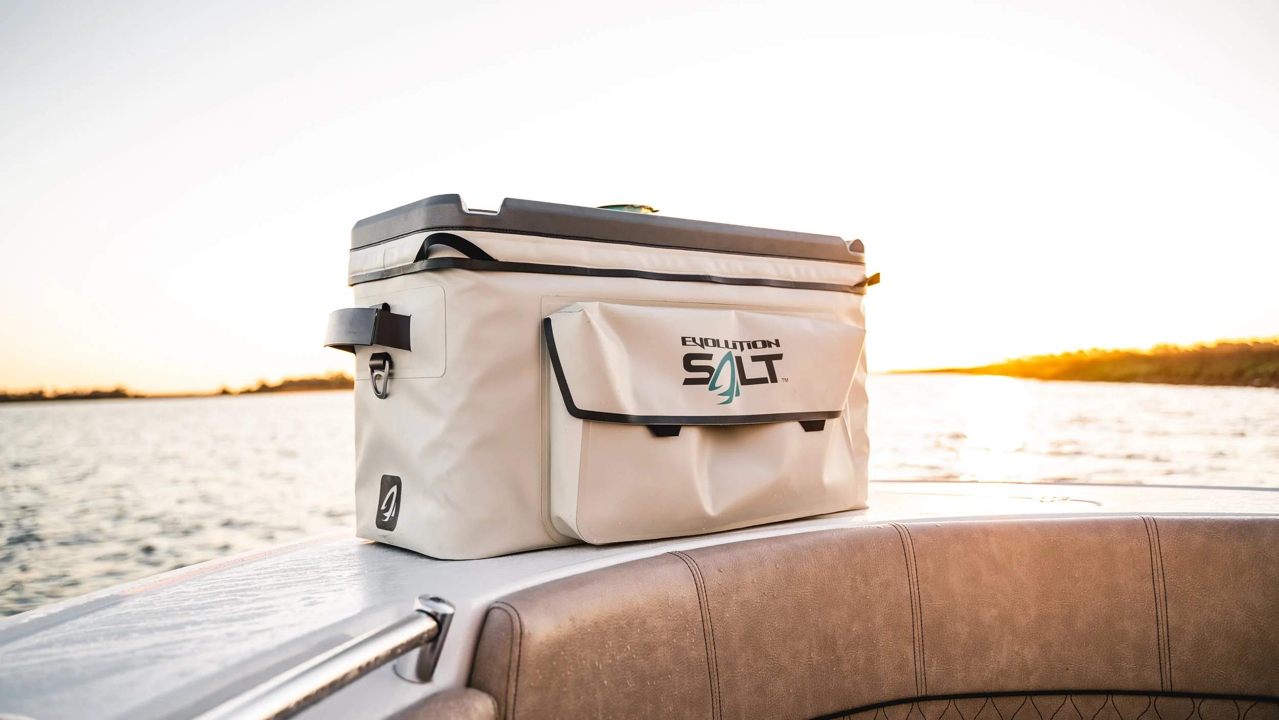 A white cooler with the words 'Evolution Salt' printed on it, placed on the edge of a boat at sunset.