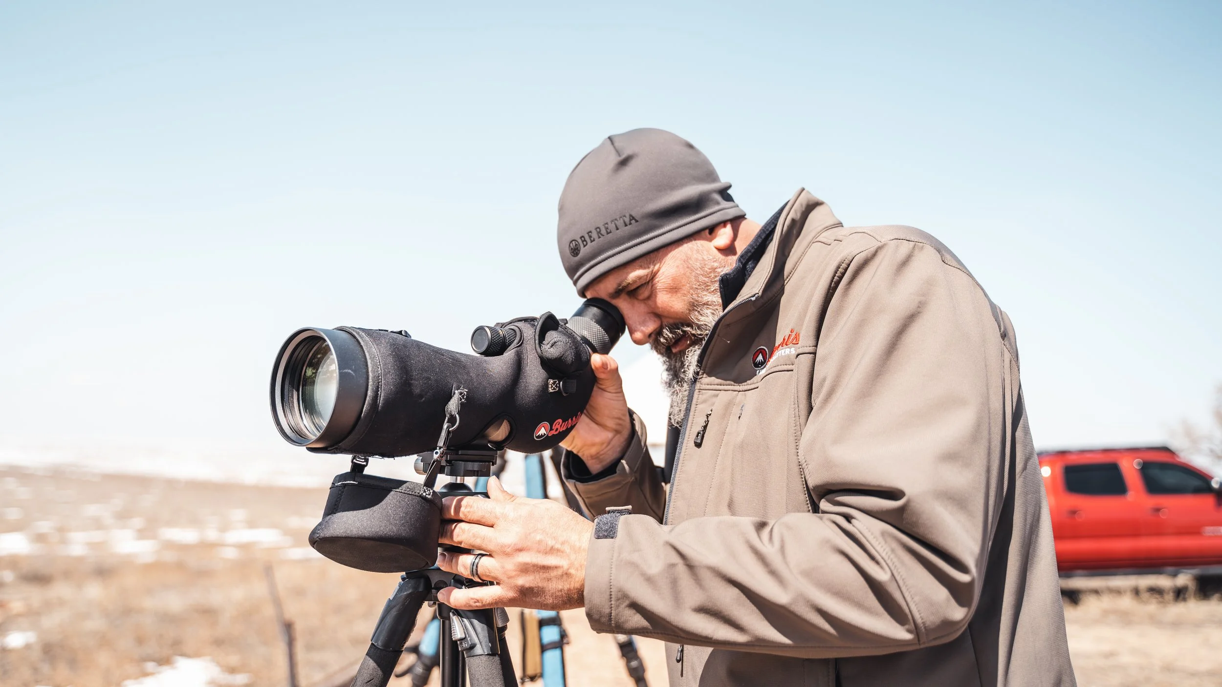 A man looking through a spotting scope outdoors on a bright day.