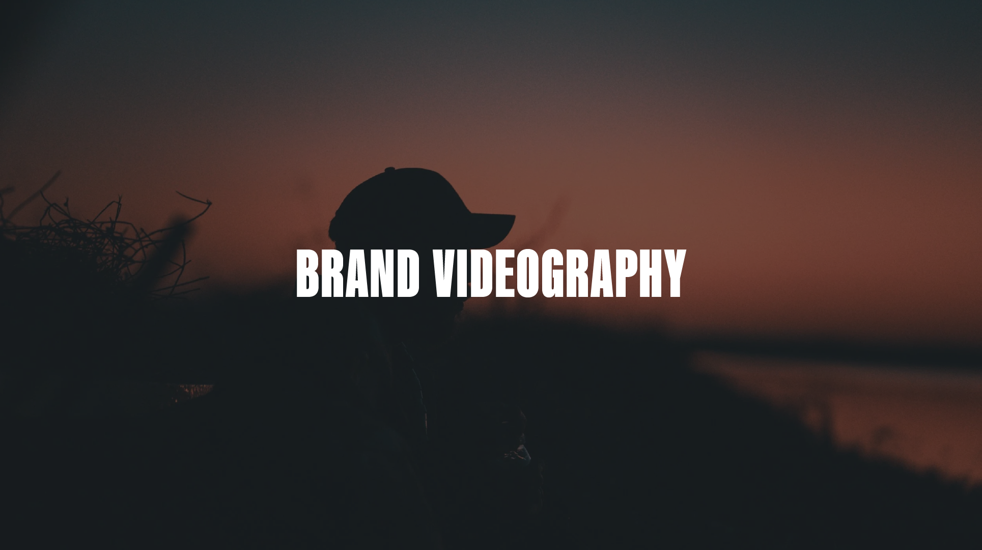 Silhouette of a person wearing a cap with a natural landscape and setting sun in the background, overlaid with the text 'Brand Videography'.