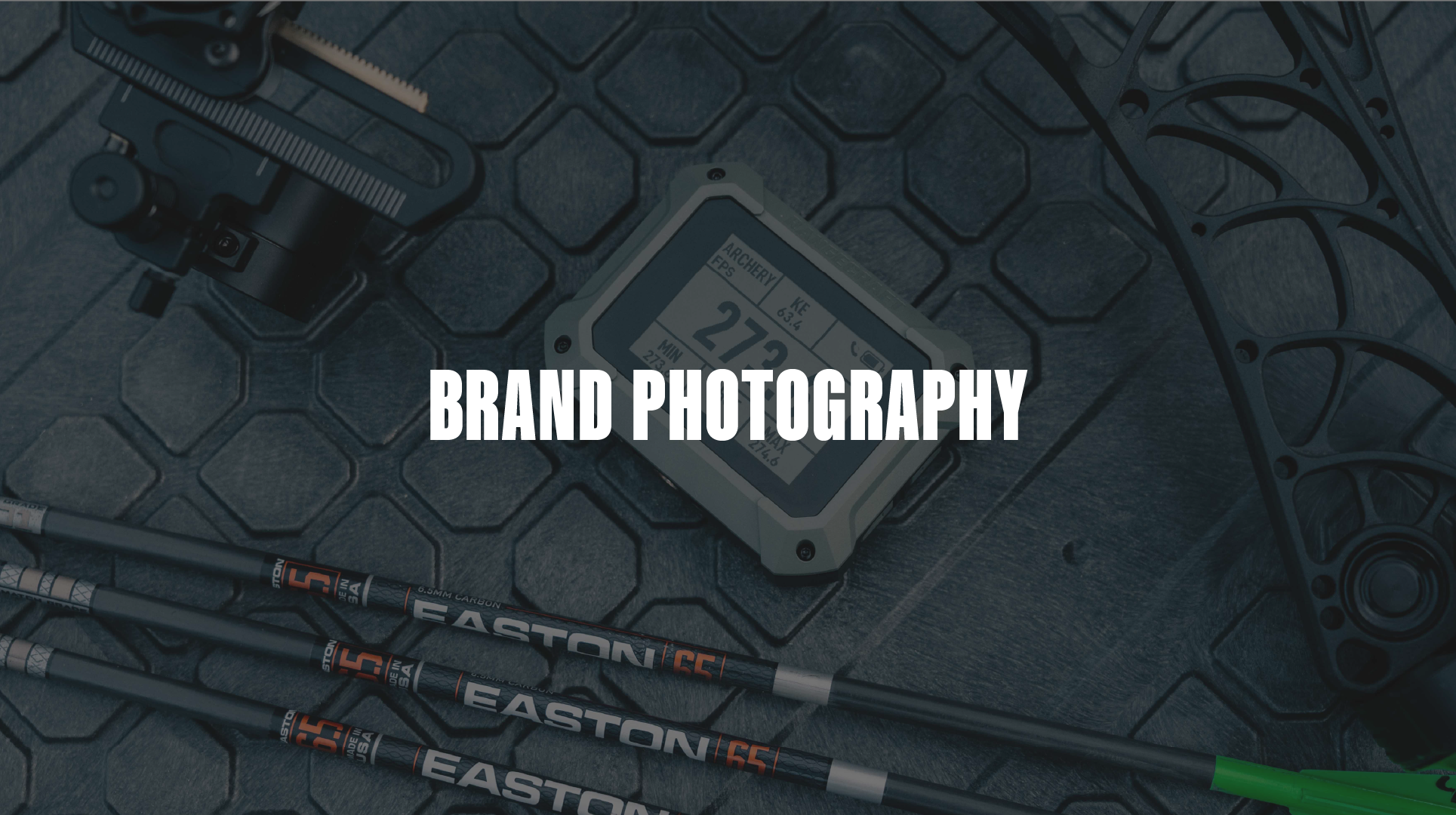 Archery equipment including a digital rangefinder, three Easton archery arrows, a bow sight, and a bow string on a textured surface.