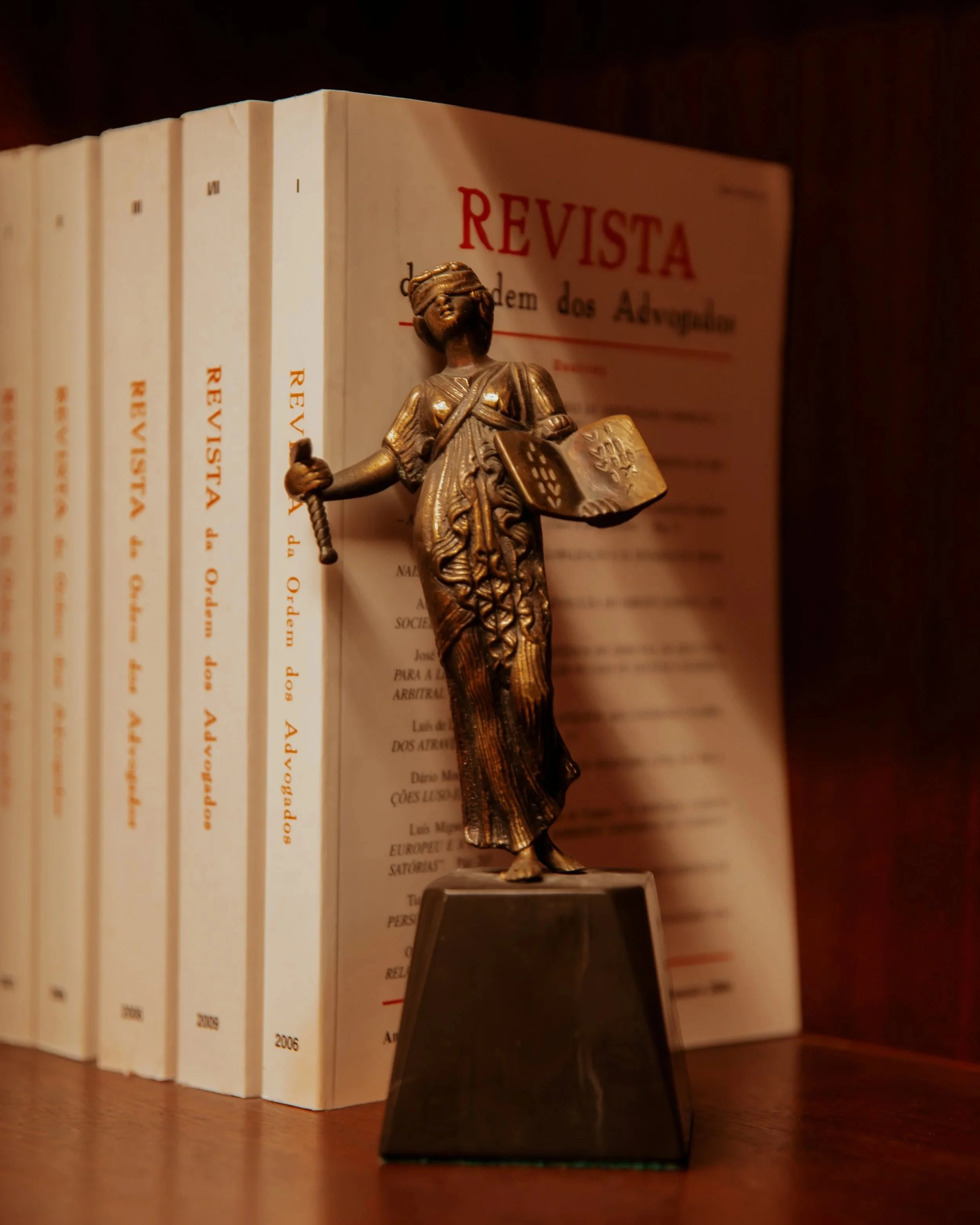Estatueta de uma mulher segurando uma bola de basquete, colocada sobre uma base preta, com livros ao fundo. Fernando Anastácio e Associados