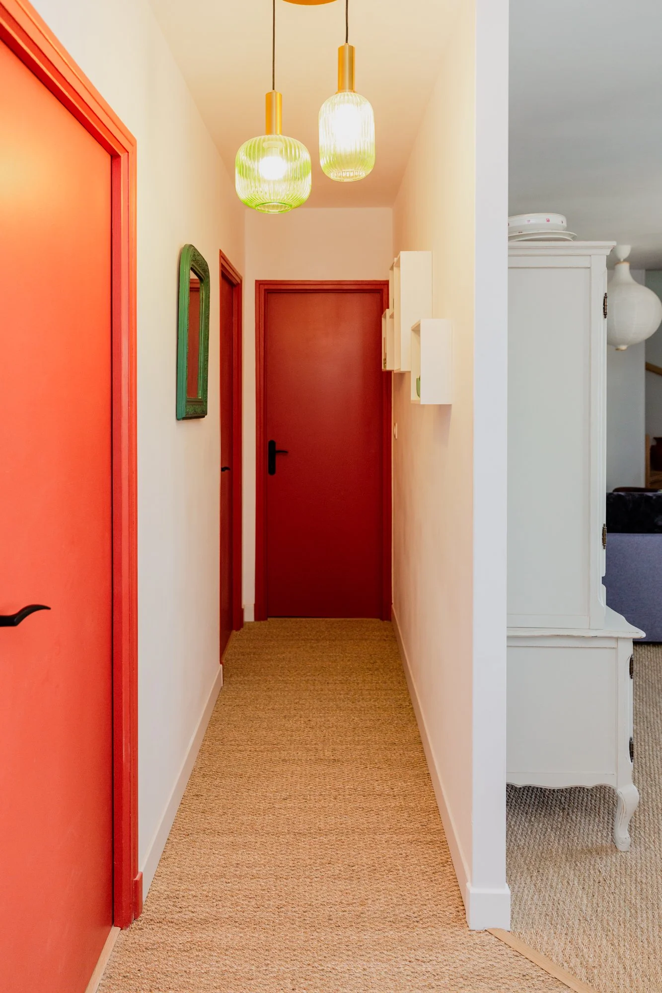 Colorful home hallway with red doors, pendant lights, a green-framed mirror, and beige carpet