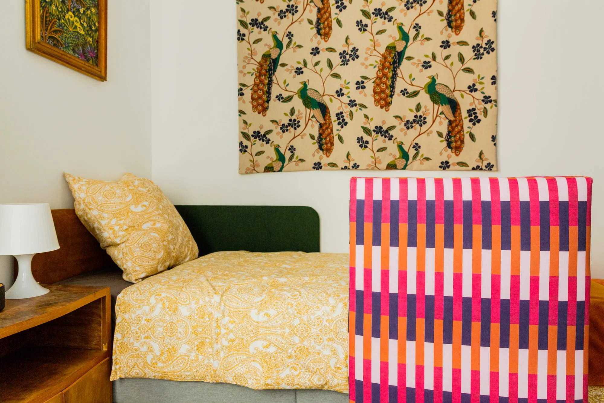 Colorful bedroom with a paisley bedspread, geometric blanket, peacock wall art, patterned pillow, and bedside lamp